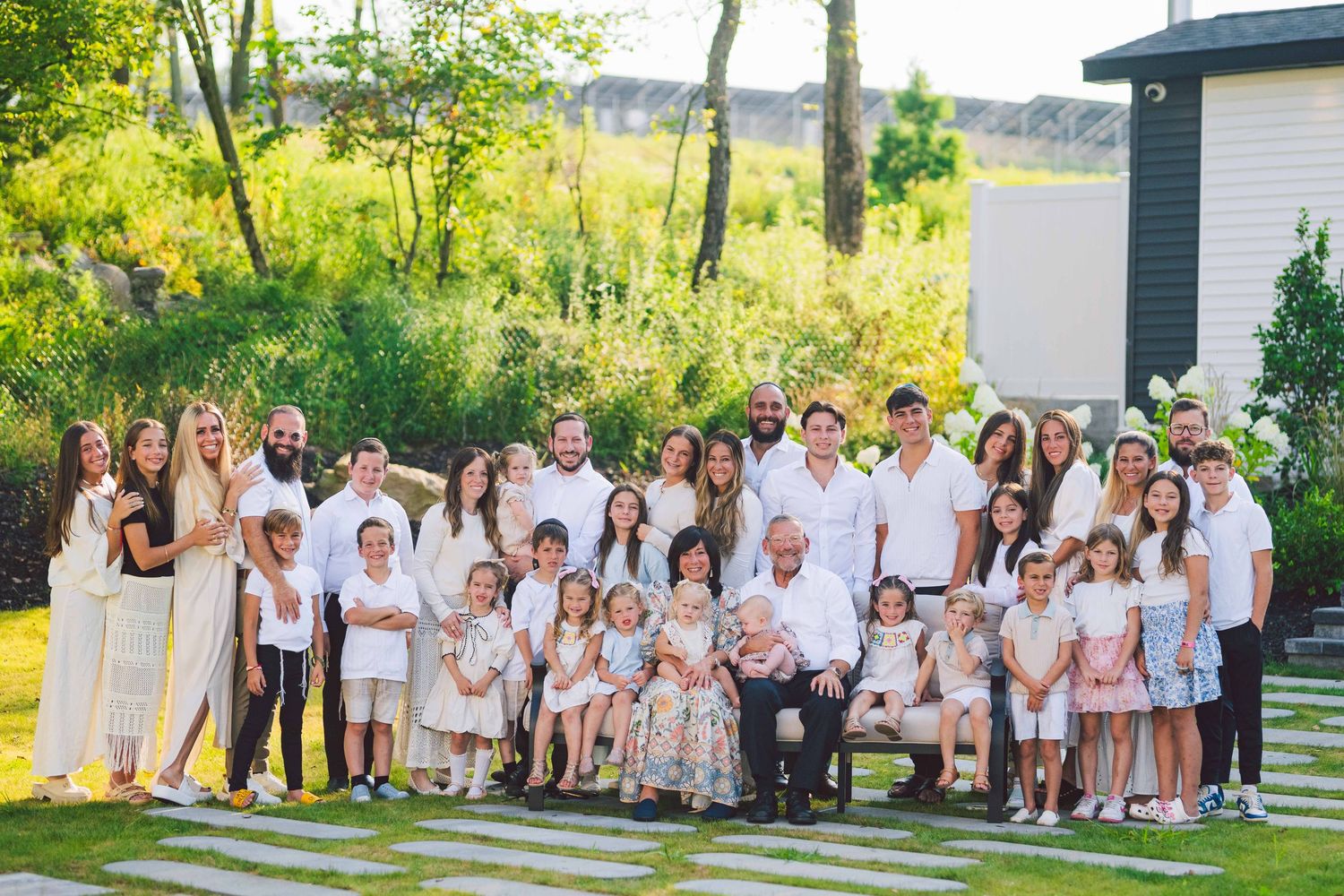 Large family group photo with everyone dressed in white and beige outfits on a sunny summer day.
