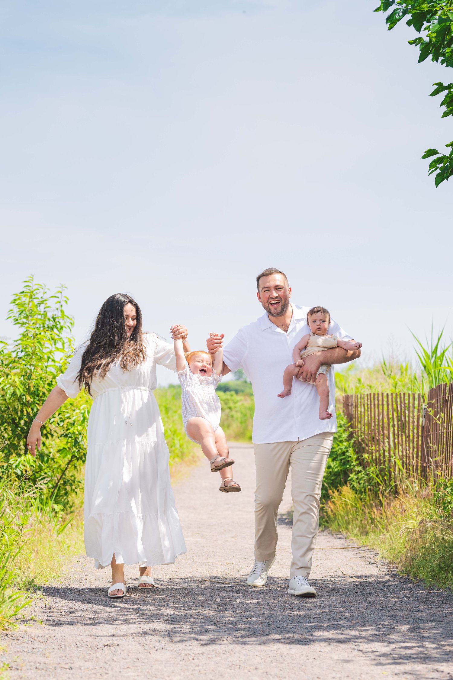 A playful family photoshoot sequence on a gravel path with coordinated white and beige outfits.