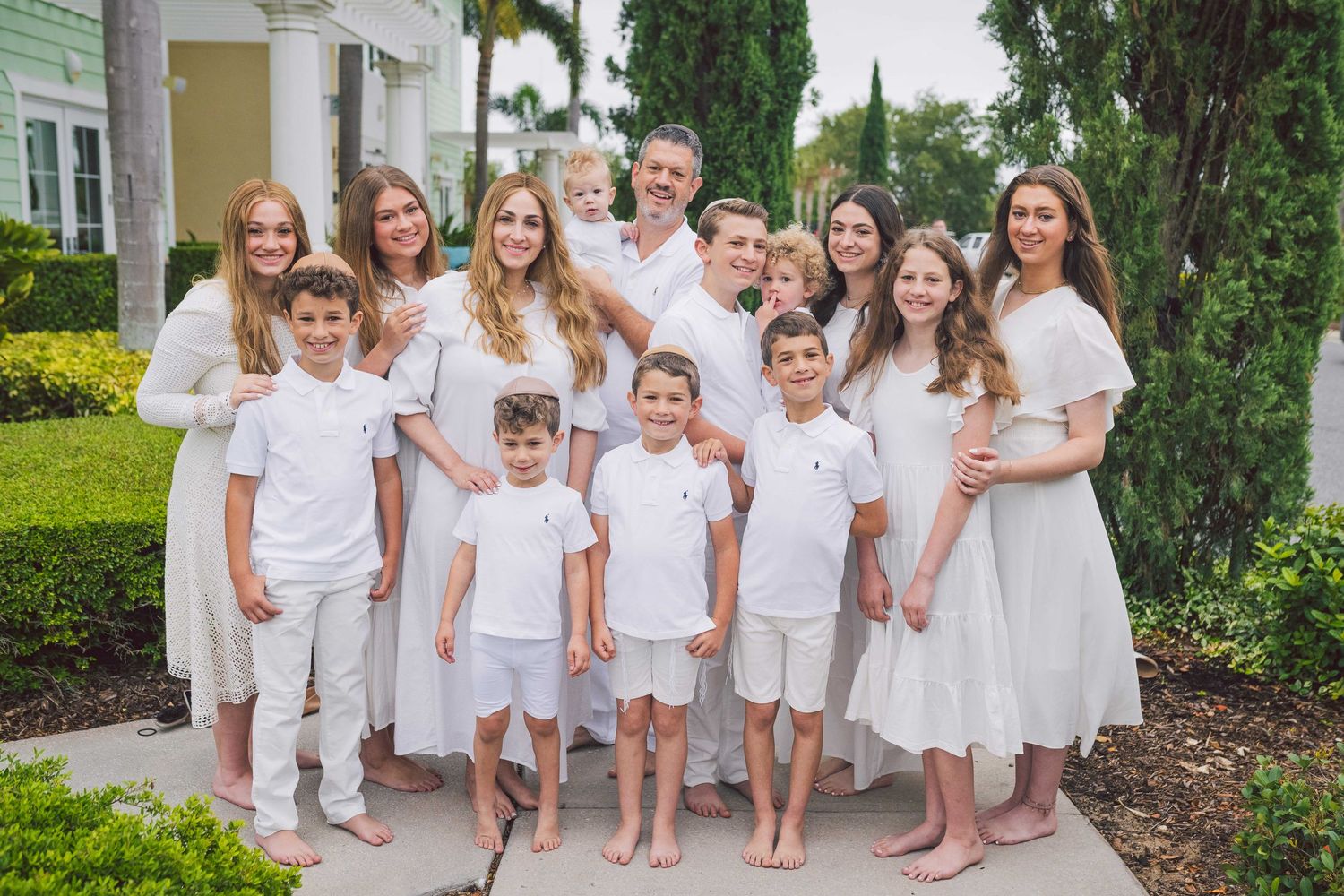 Large group portrait of children in coordinating white outfits posed together outdoors.