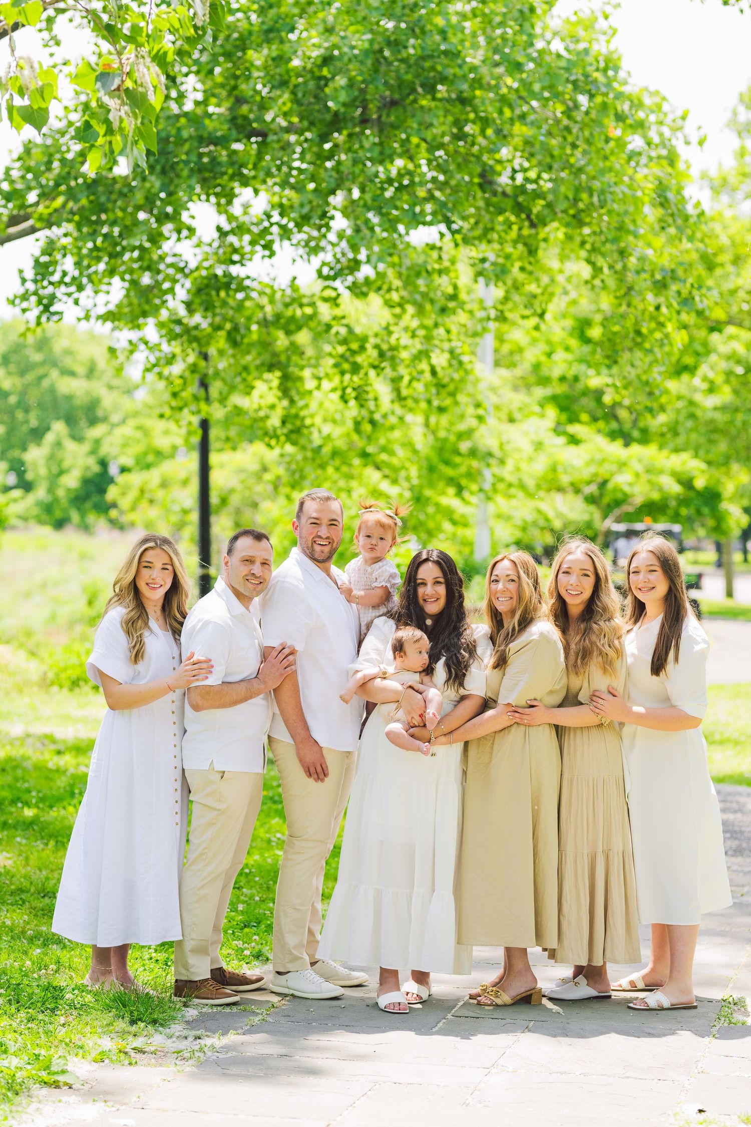 Extended family group portrait in coordinating white and beige outfits posed outdoors.