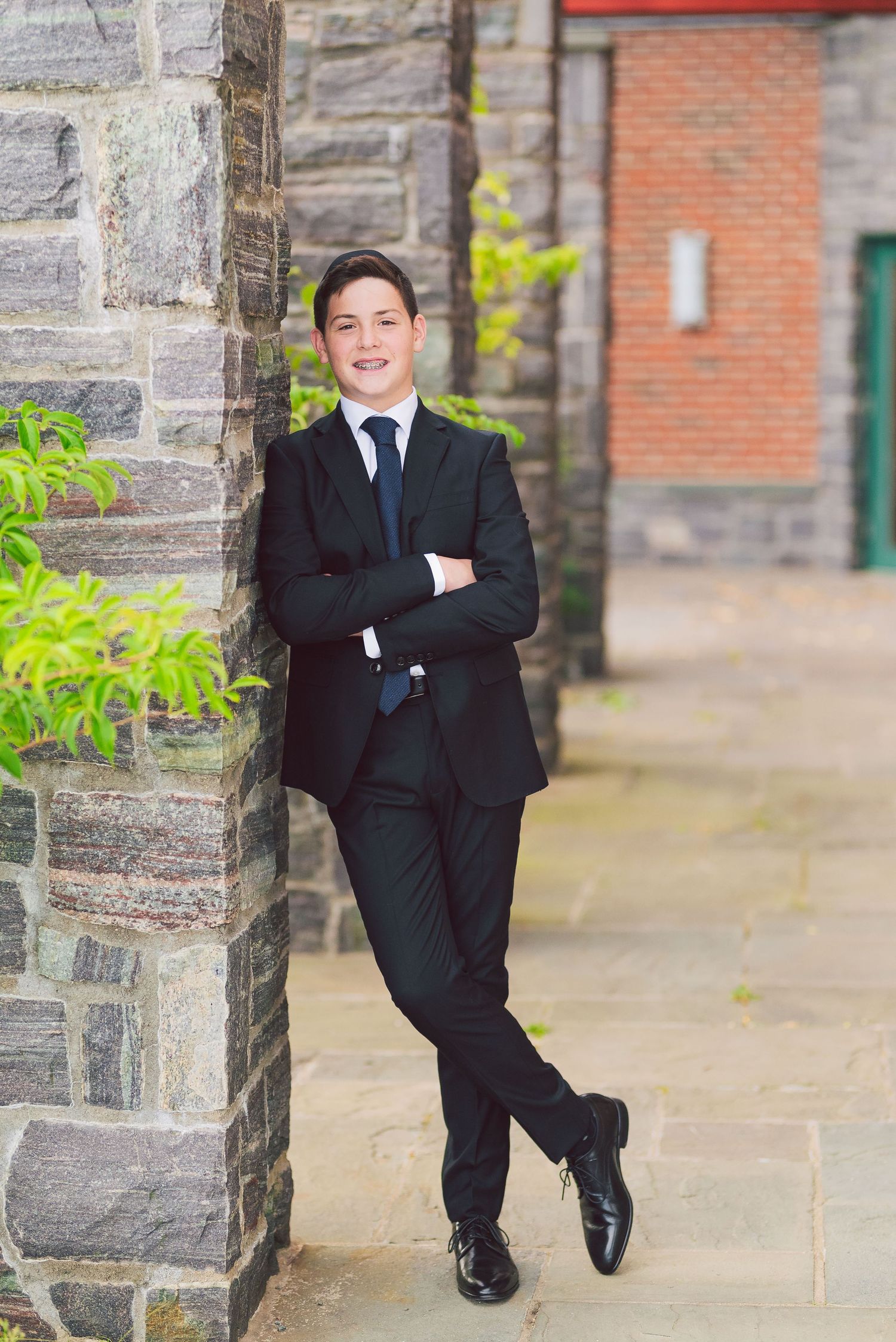 Person in black suit posing against stone wall in professional portrait.