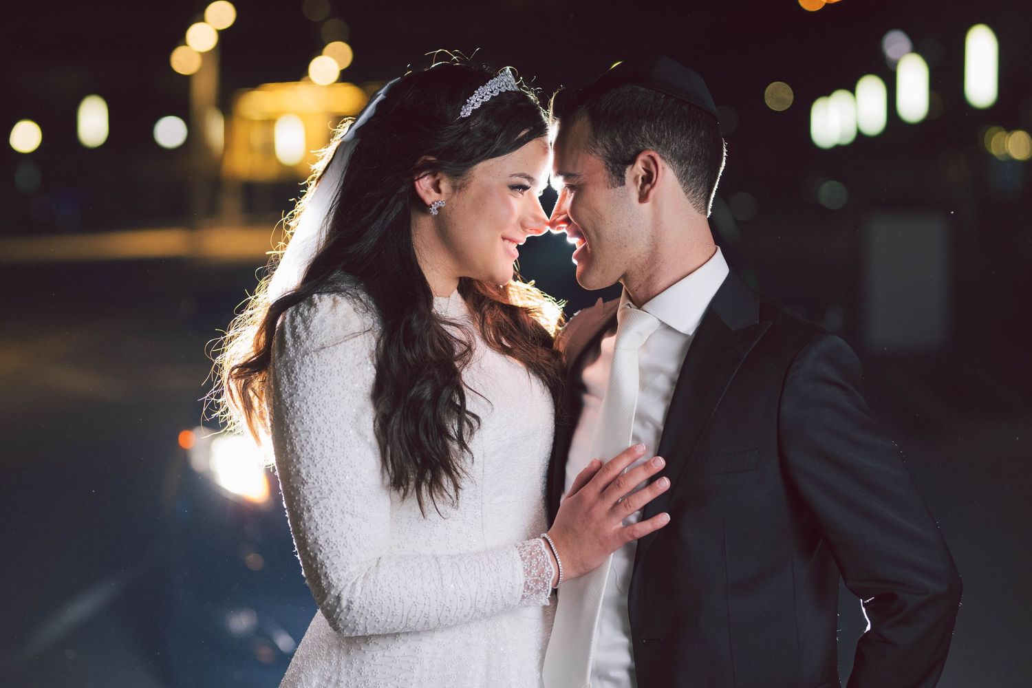 Romantic nighttime wedding portrait with city lights in background.
