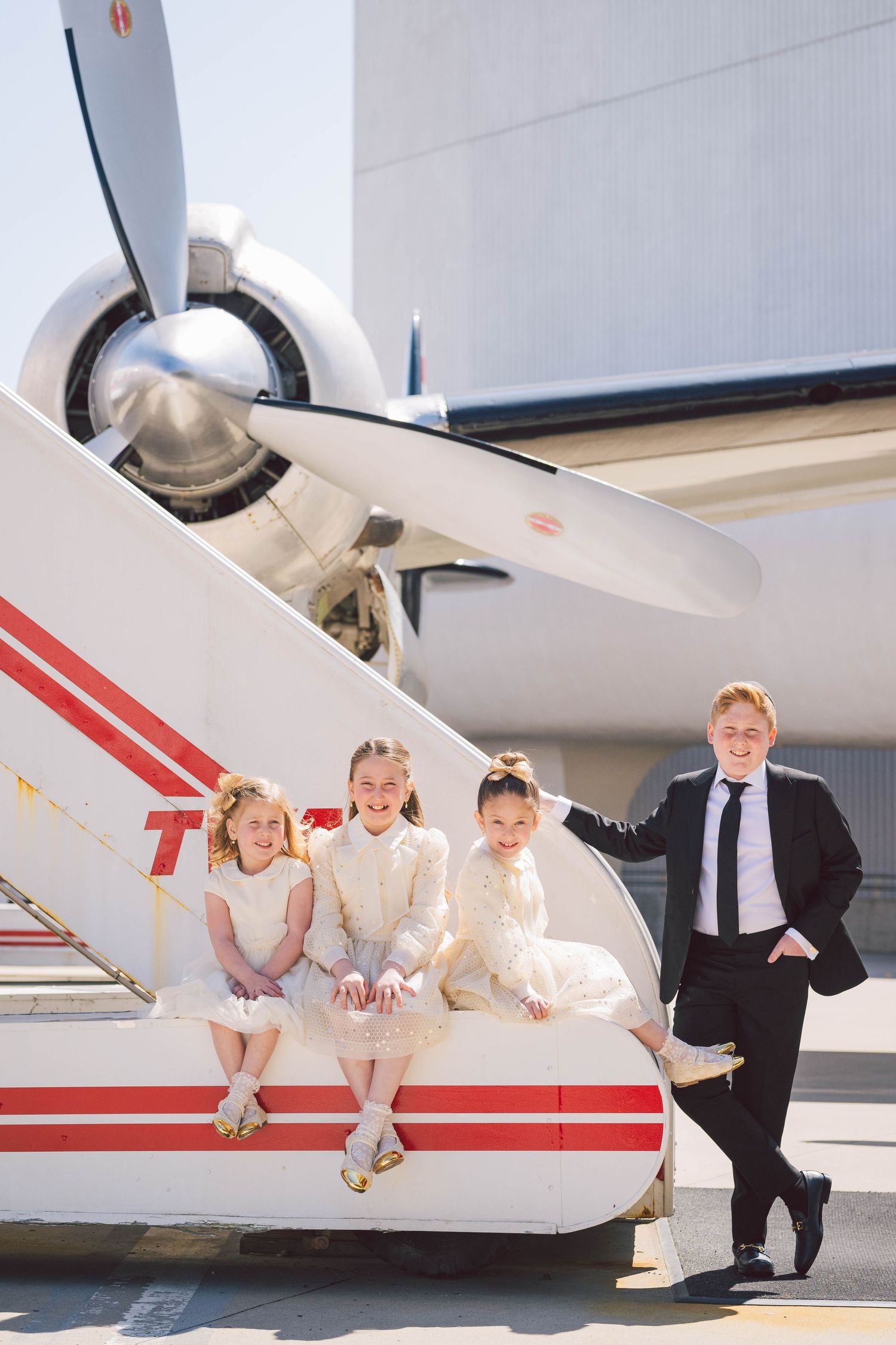 Three children and adult posing by vintage propeller aircraft wing.