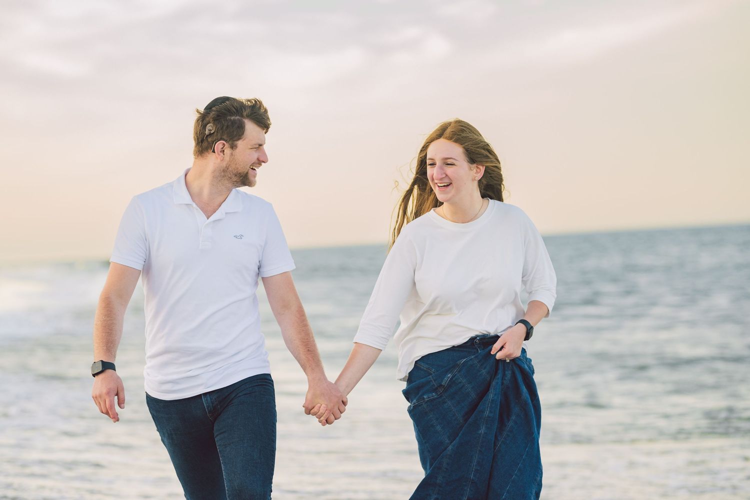 Happy couple walking and laughing together on a beach in casual summer outfits.