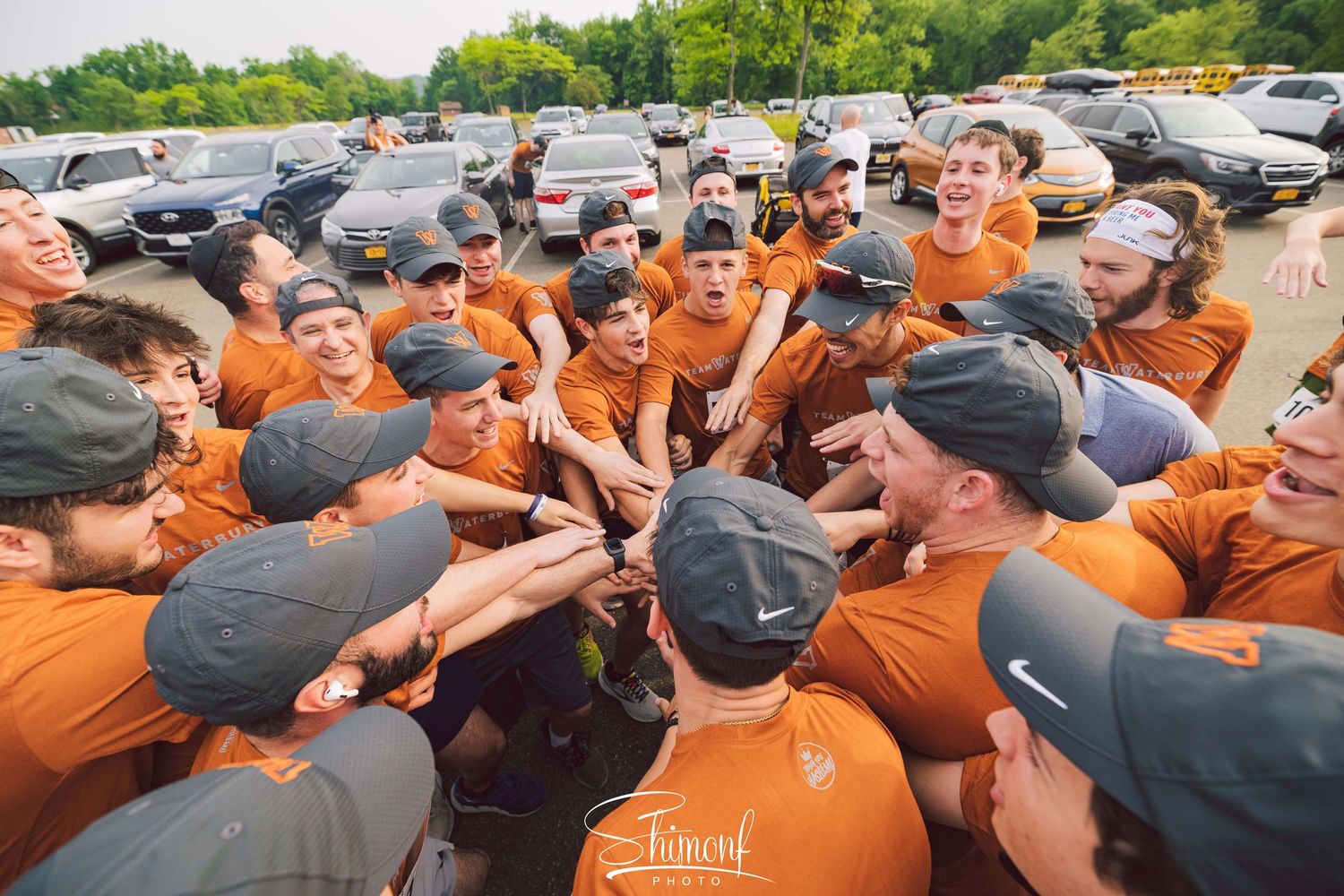 Group of people in orange shirts huddle together during outdoor team event.