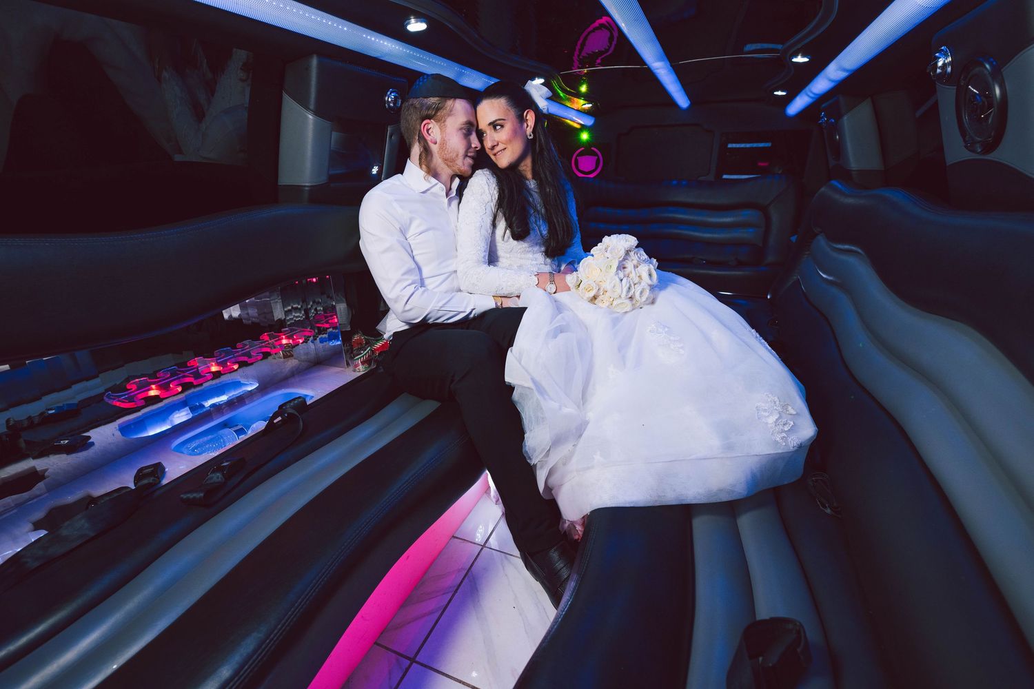 Newlywed couple sharing romantic moments inside a limousine with colorful lighting.