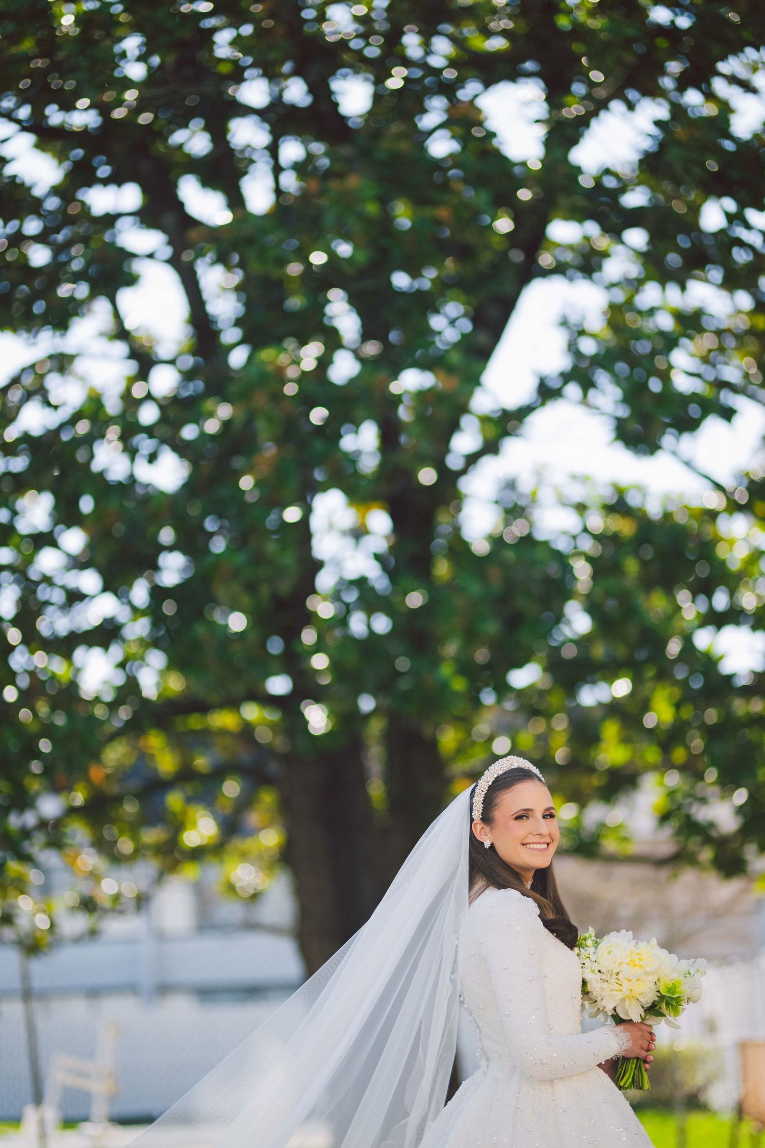 Beautiful wedding photo with flowing veil against natural outdoor backdrop.