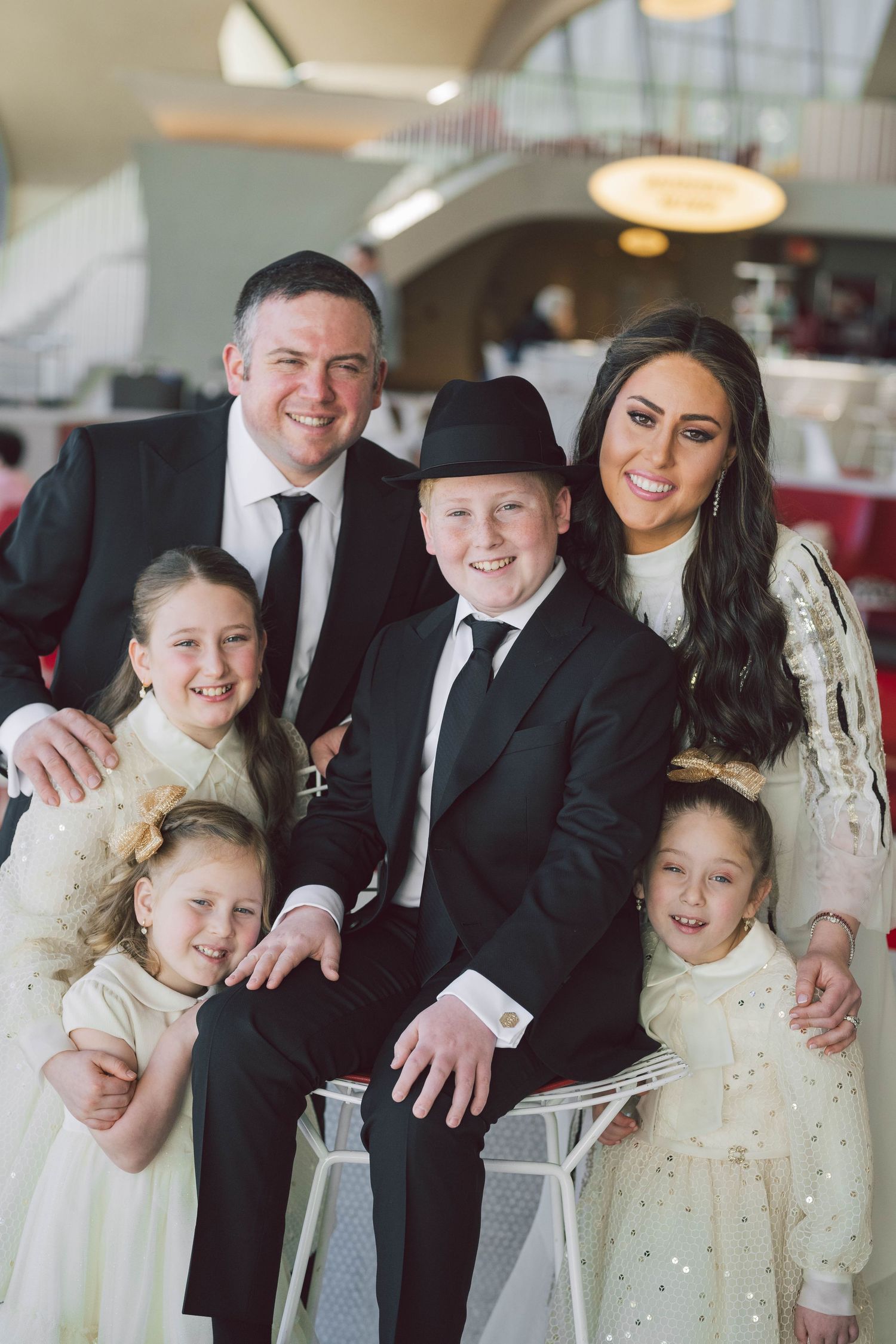Family portrait featuring parents and three children dressed in formal attire seated together indoors.