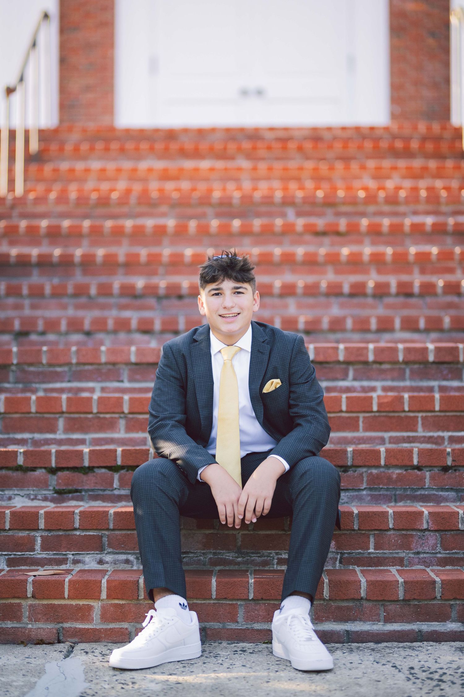 Fashionably dressed person sitting on brick steps wearing a dark suit and yellow tie.
