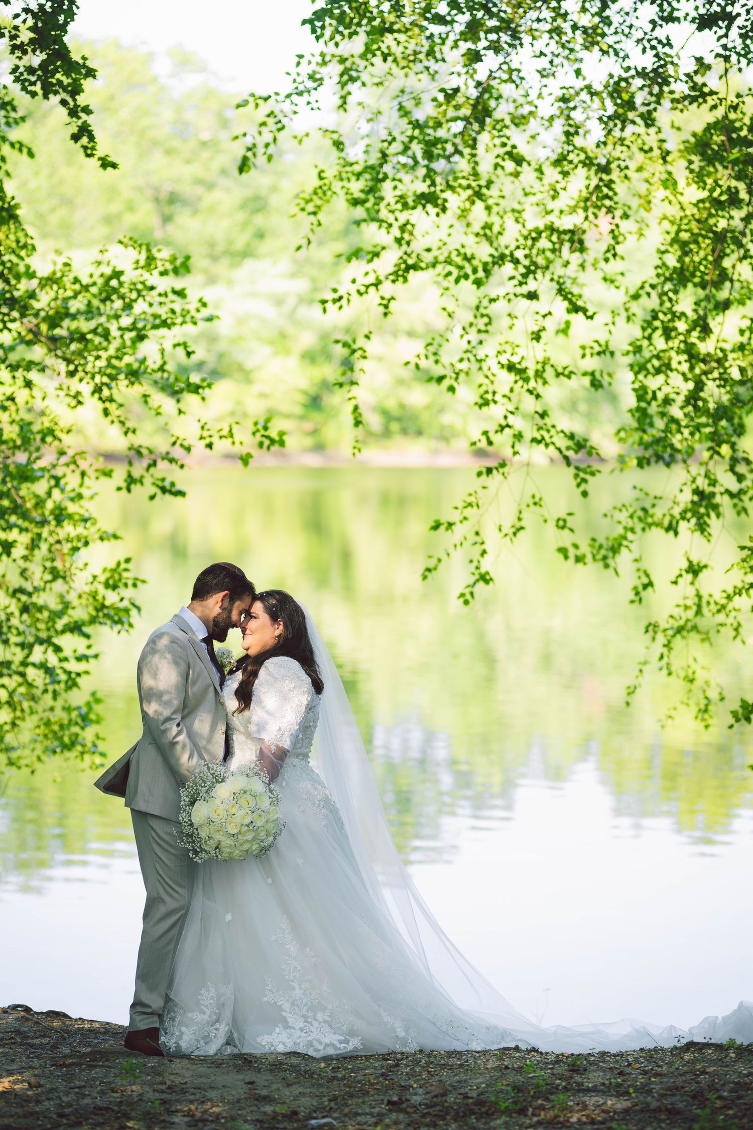 Romantic wedding photos by a lake with overhanging tree branches creating natural framing.