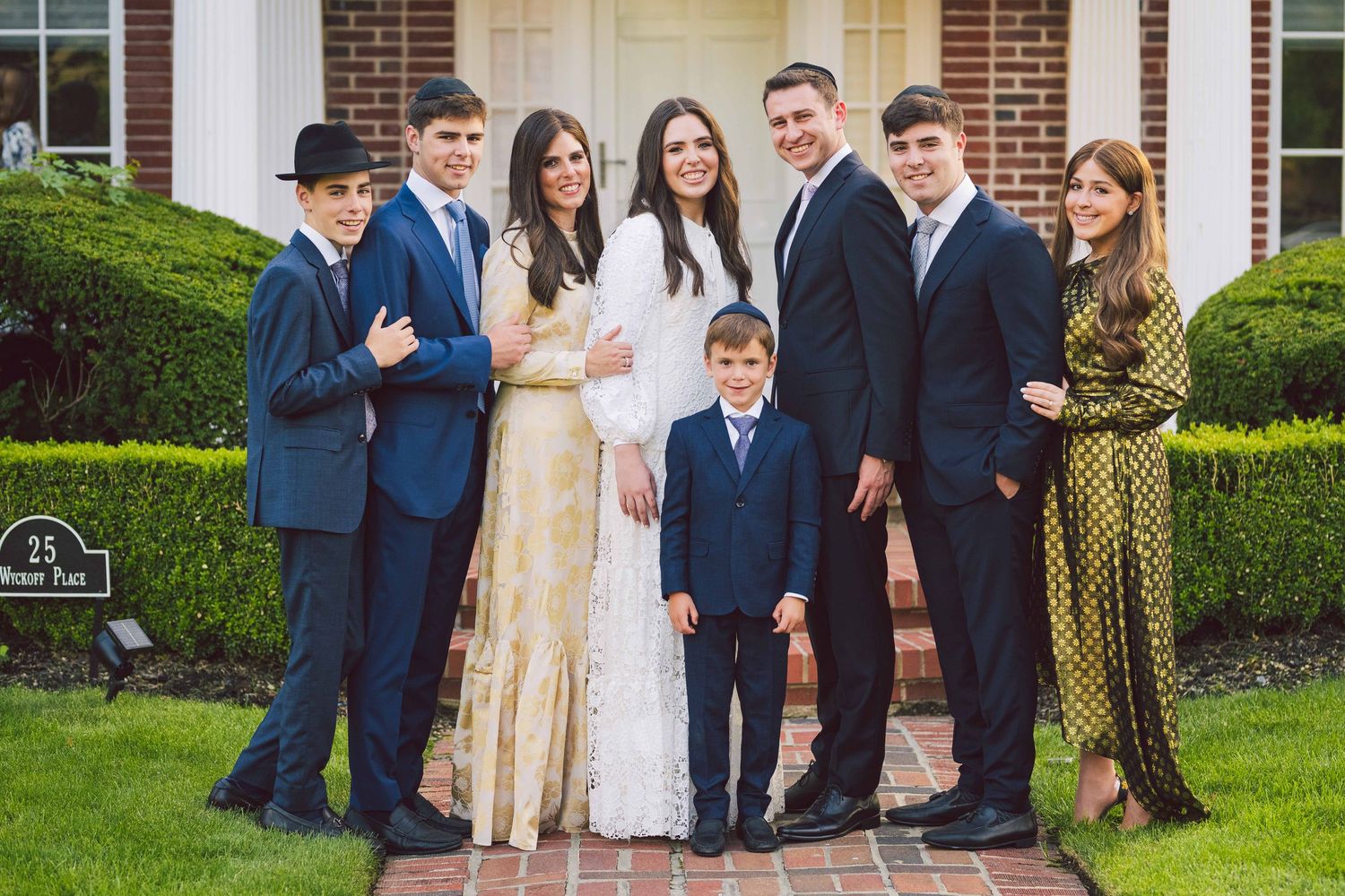 Group photo of wedding party in navy suits and gold dresses gathered outside brick building.