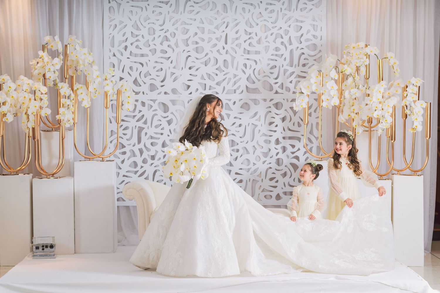 Bridal portrait in elegant white ballgown amid gold candelabras and white decor.
