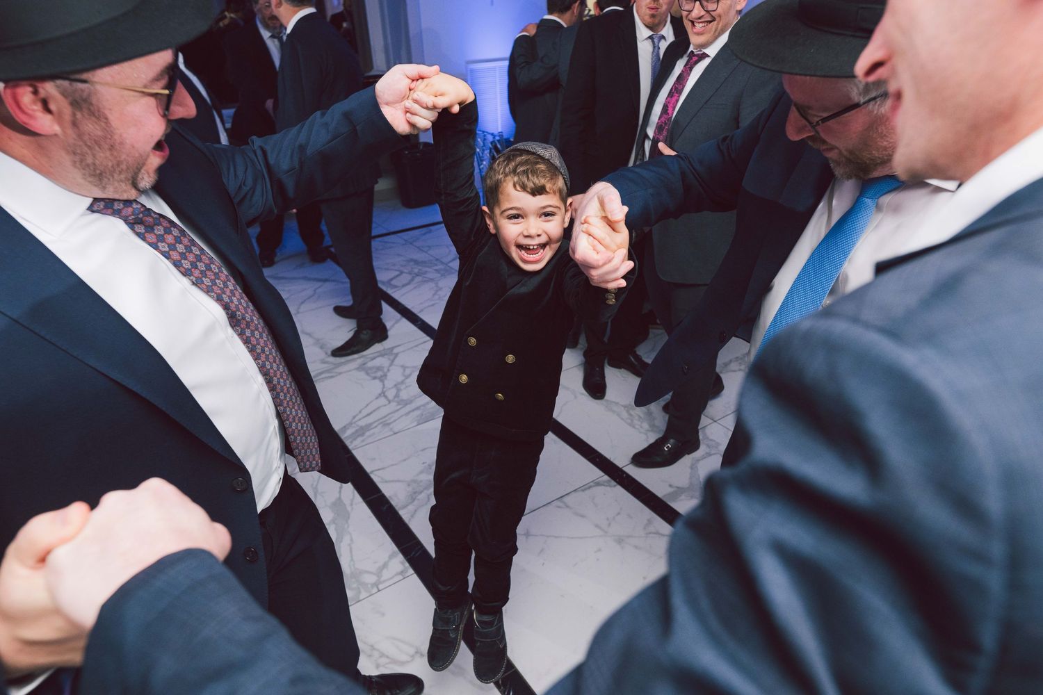 Guests dancing and celebrating at a wedding reception with blue lighting and formal attire.