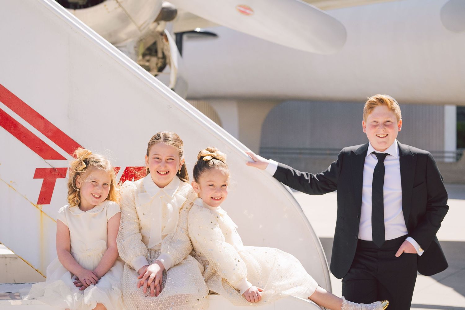 Kids in formal attire gather beside a aircraft
