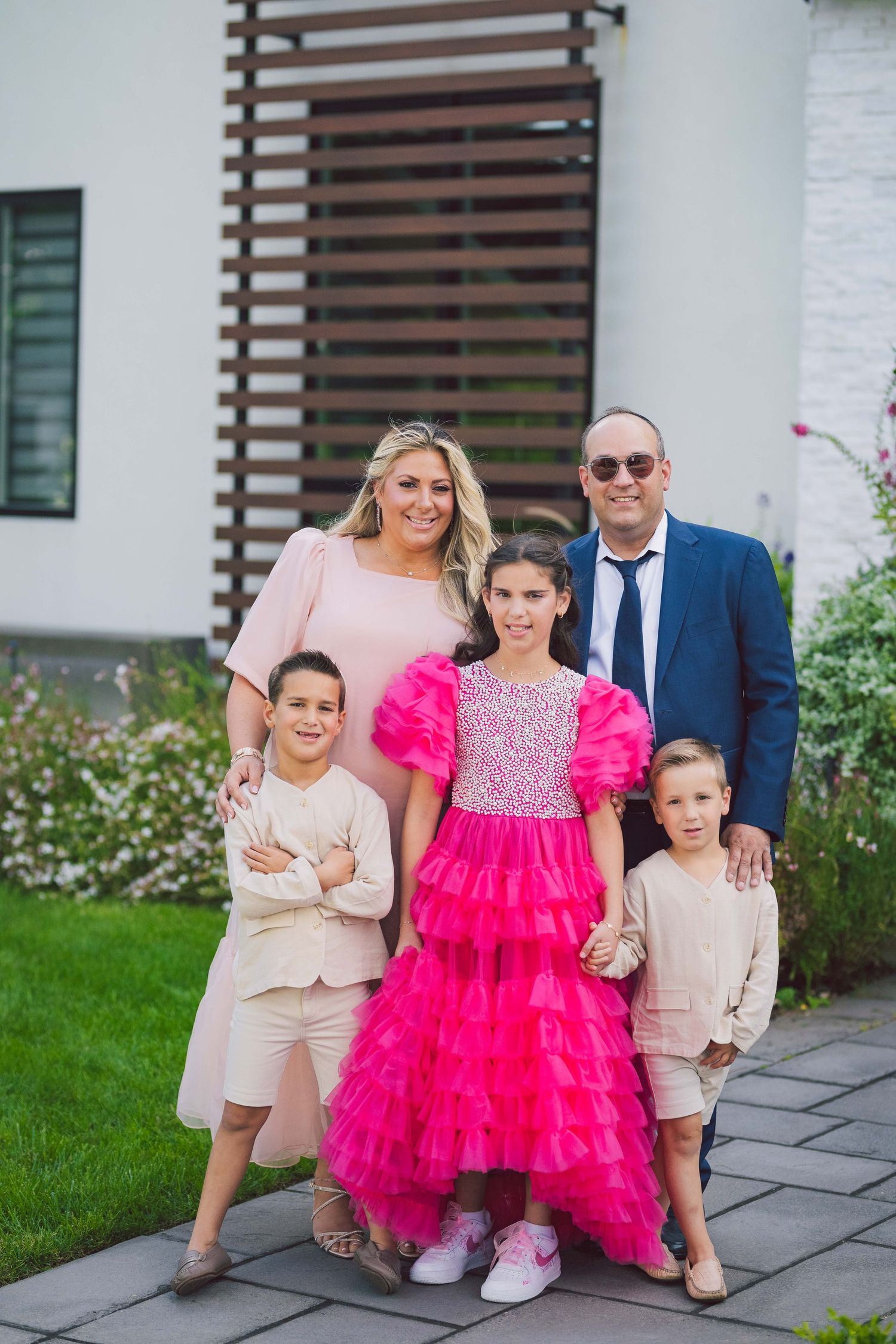 Family portrait featuring a bright hot pink tulle dress and beige coordinated outfits in an outdoor garden setting.
