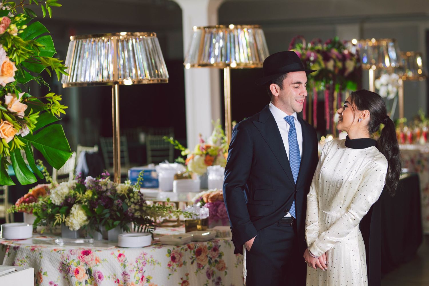 Wedding party dressed elegantly celebrating at a table decorated with floral arrangements and candles.