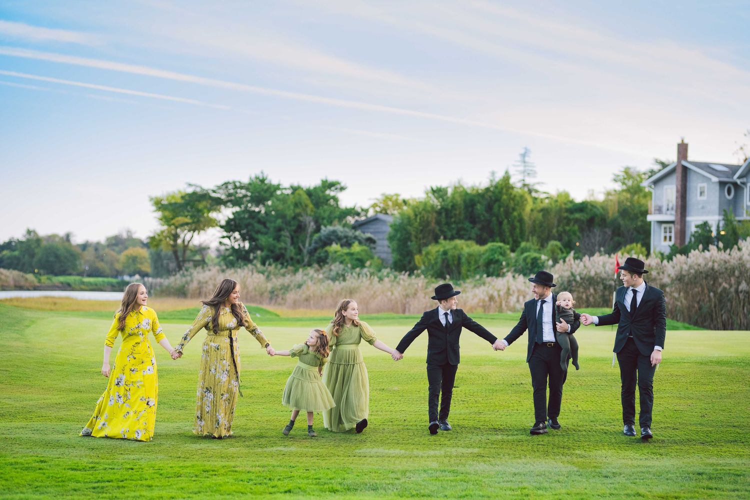 Bridal party poses creatively in a line across grassy field for fun wedding photo.