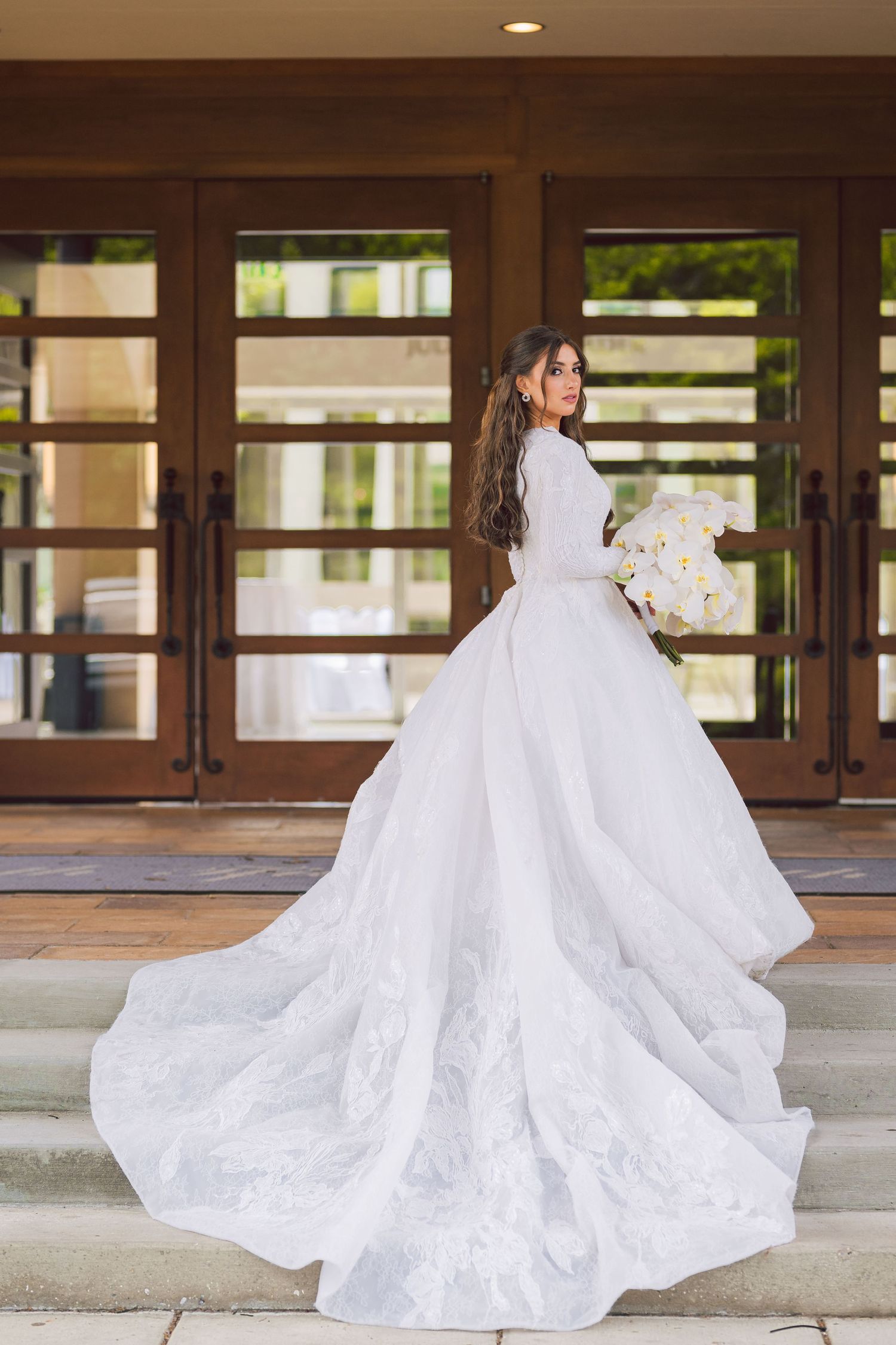 Wedding gown with dramatic long train photographed outdoors against wooden doors.