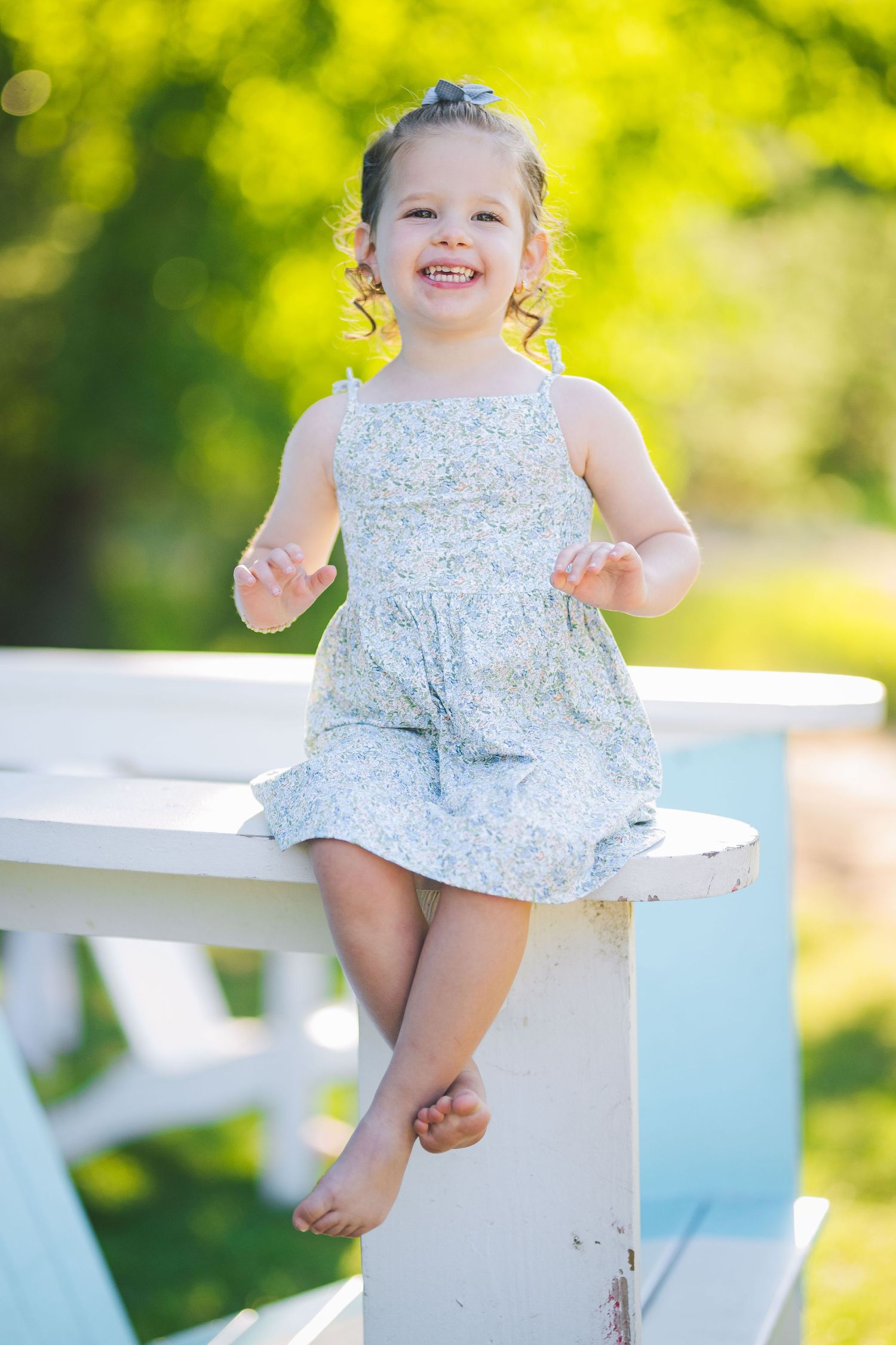 A series of joyful shots showing a small child in a floral dress sitting on a white bench.