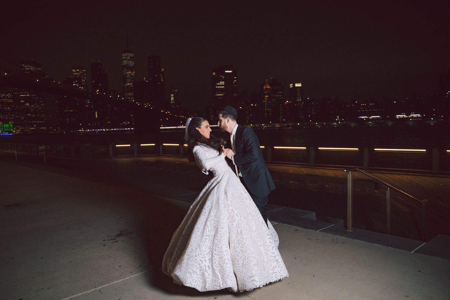 Elegant wedding couple dances under city lights at night.