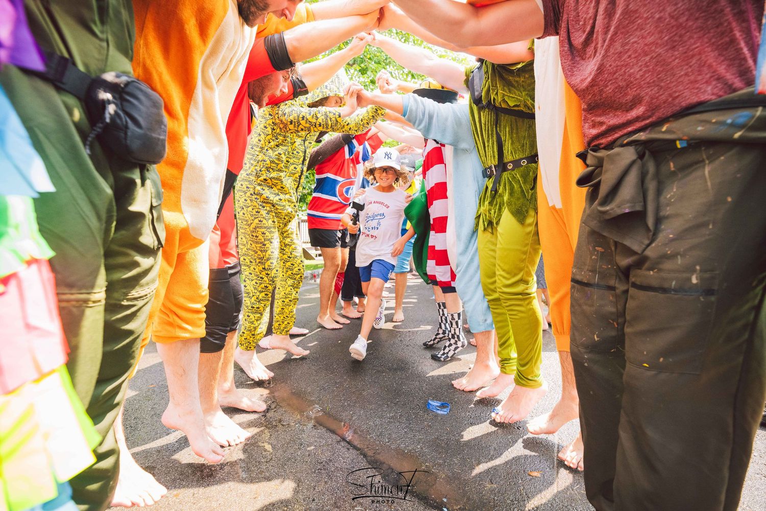 Wedding guests' feet and legs shown in bright, colorful outfits during outdoor celebration.