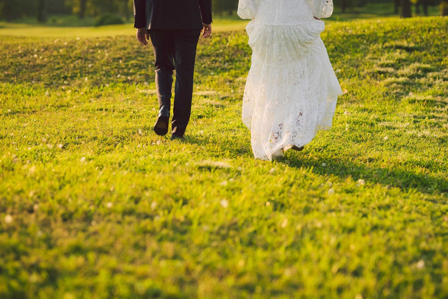 Couple walking together on grassy lawn during golden hour photoshoot.