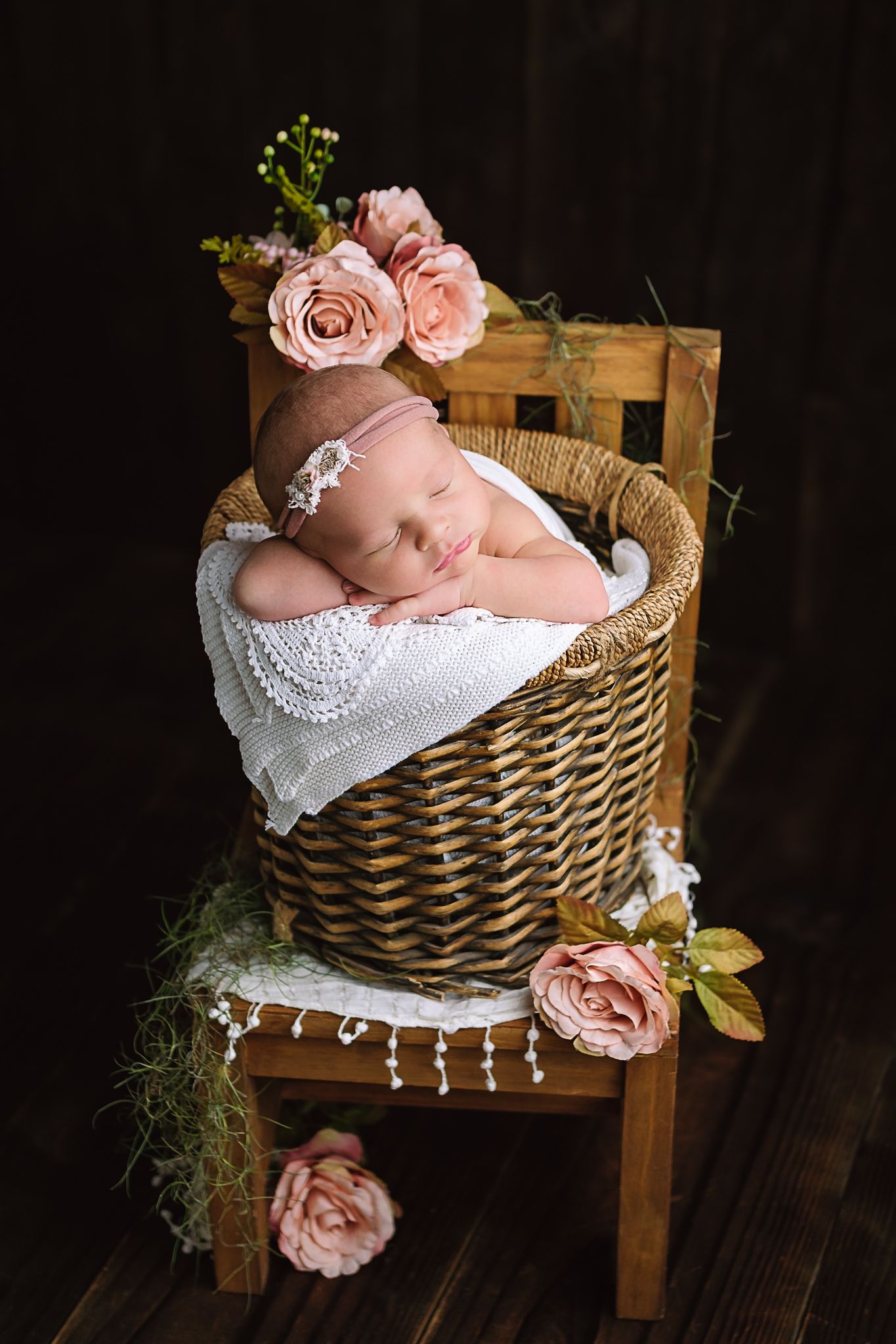 Newborn baby posed in a basket with soft peach roses in studio