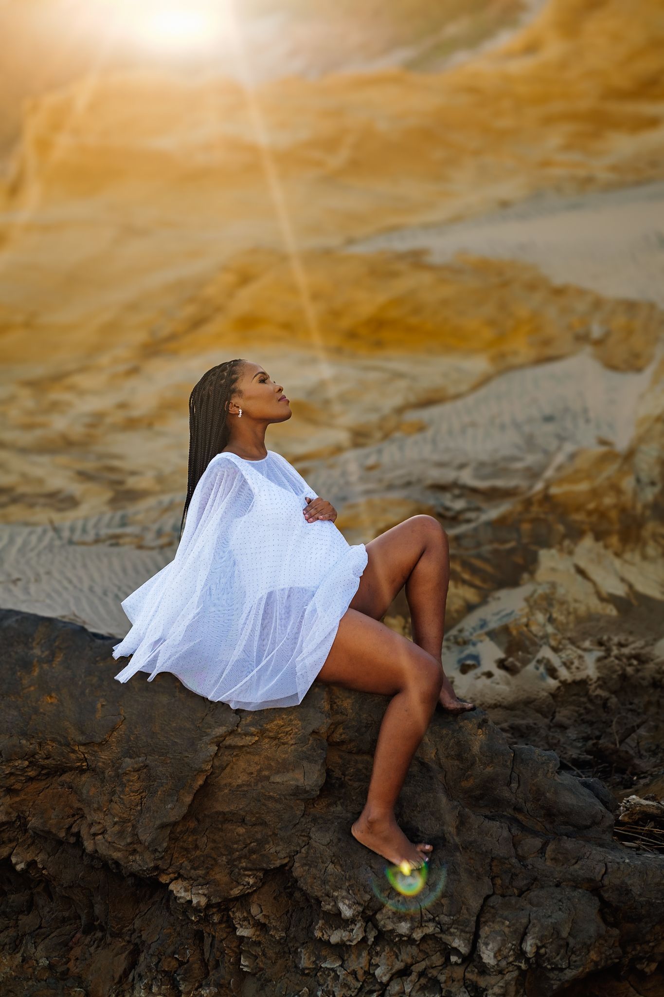 Pregnant woman sitting on a rock at the beach during a maternity photoshoot