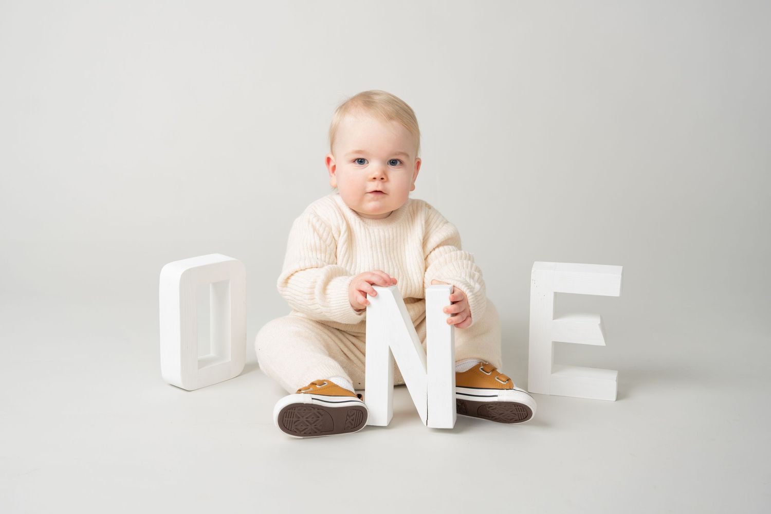 Baby sitting with wooden letter blocks spelling ONE on white background.