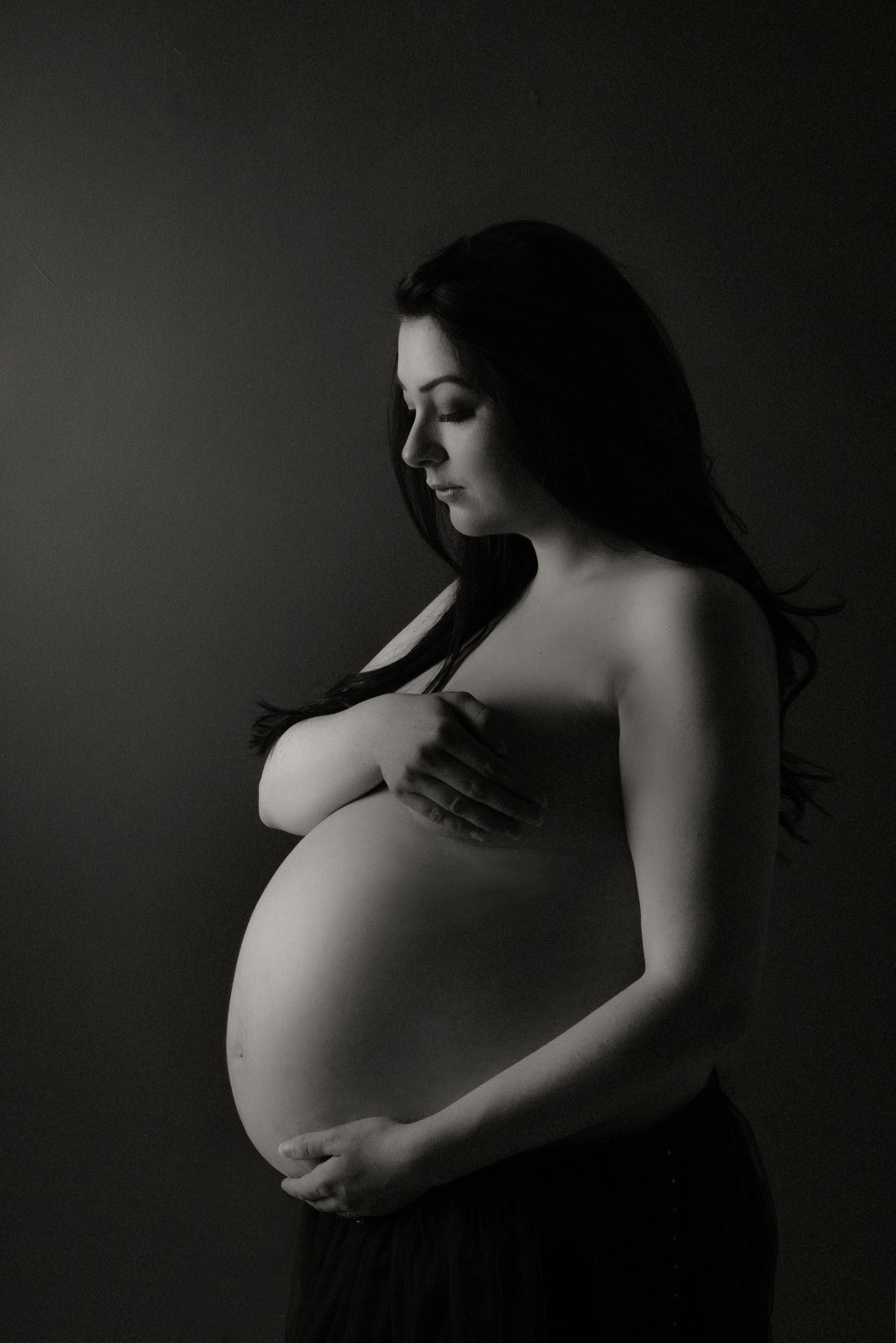Artistic black and white maternity portrait in dramatic lighting.