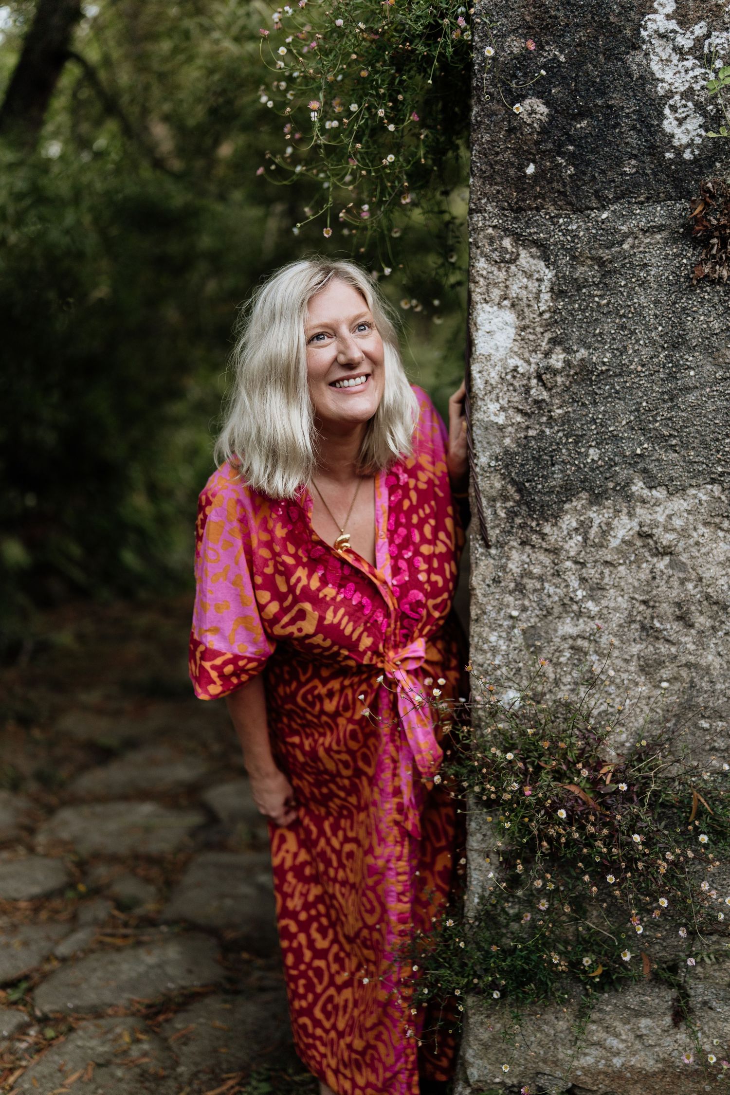 A red and pink patterned wrap dress stands out against a stone wall backdrop in a natural outdoor setting.