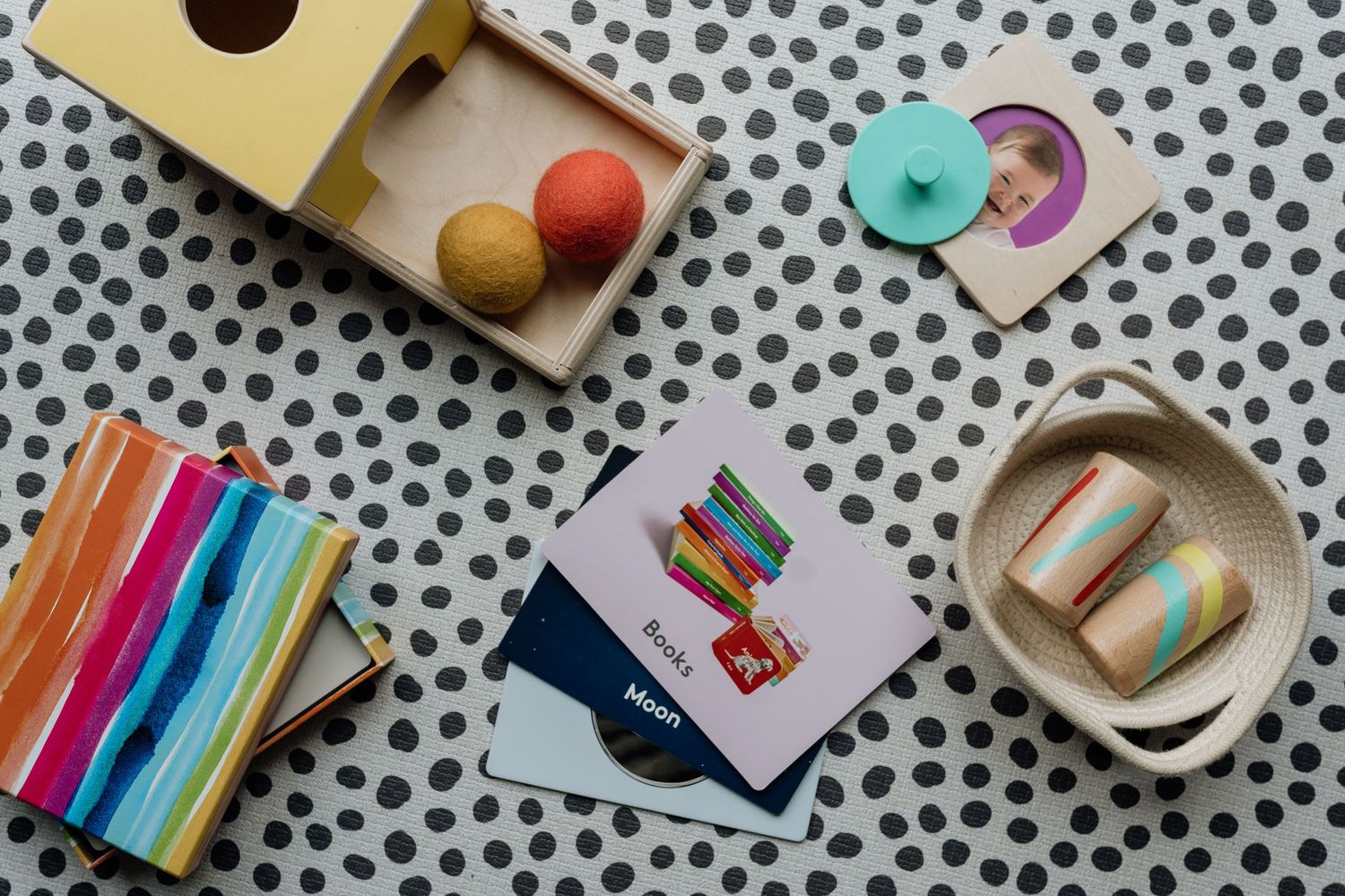 Colorful children's toys and learning materials arranged on a polka dot surface, including wooden blocks and rainbow markers.