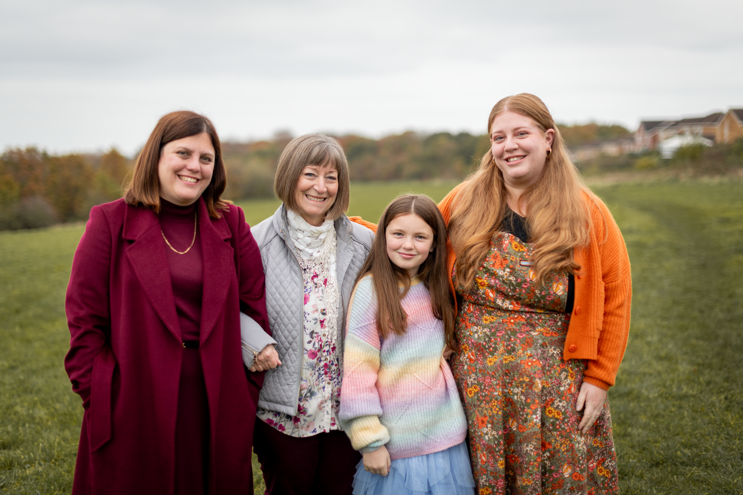 Family group in colorful coats standing together on a grassy hillside.