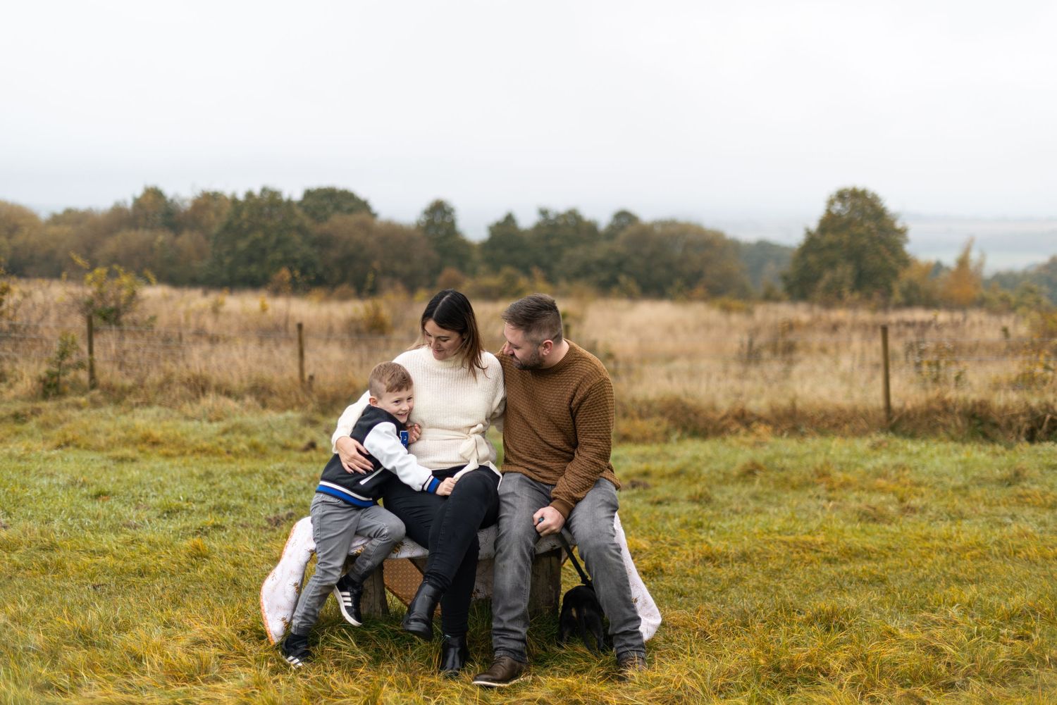 Family sitting close together on grass in a countryside setting.