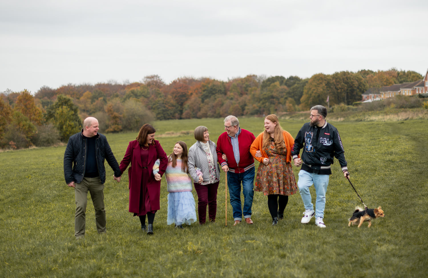 Group walking together holding hands across an autumn field with a dog.