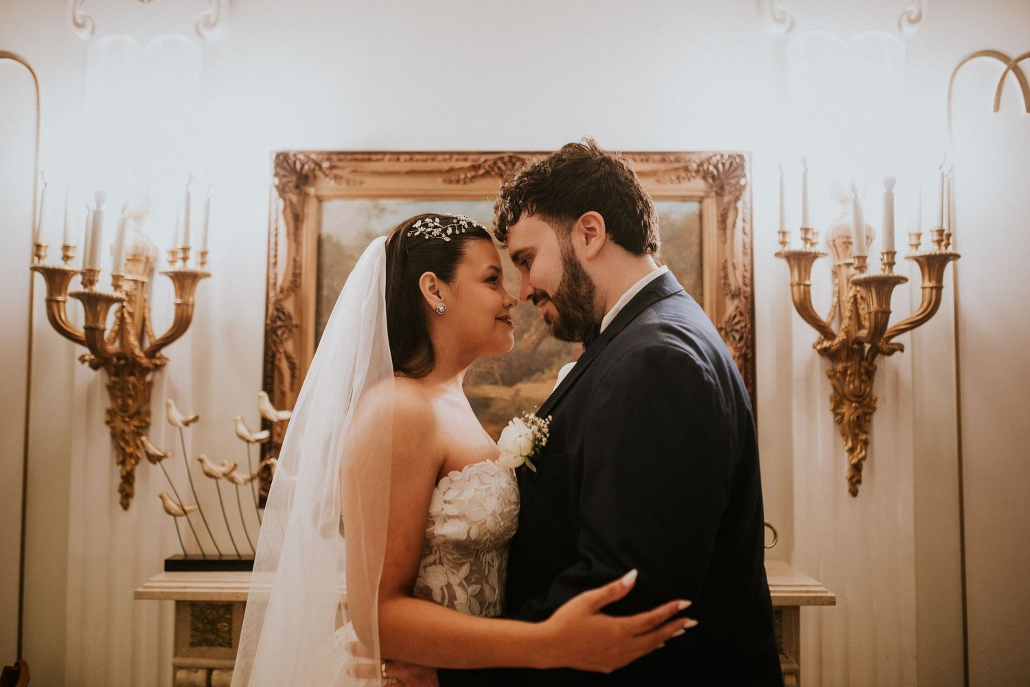 Bride and groom share an intimate moment in elegant venue with ornate gold mirror and candelabras on their wedding day.