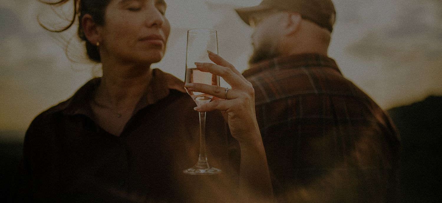 Couple toasting with champagne glasses at golden sunset, romantic outdoor celebration with warm lighting.
