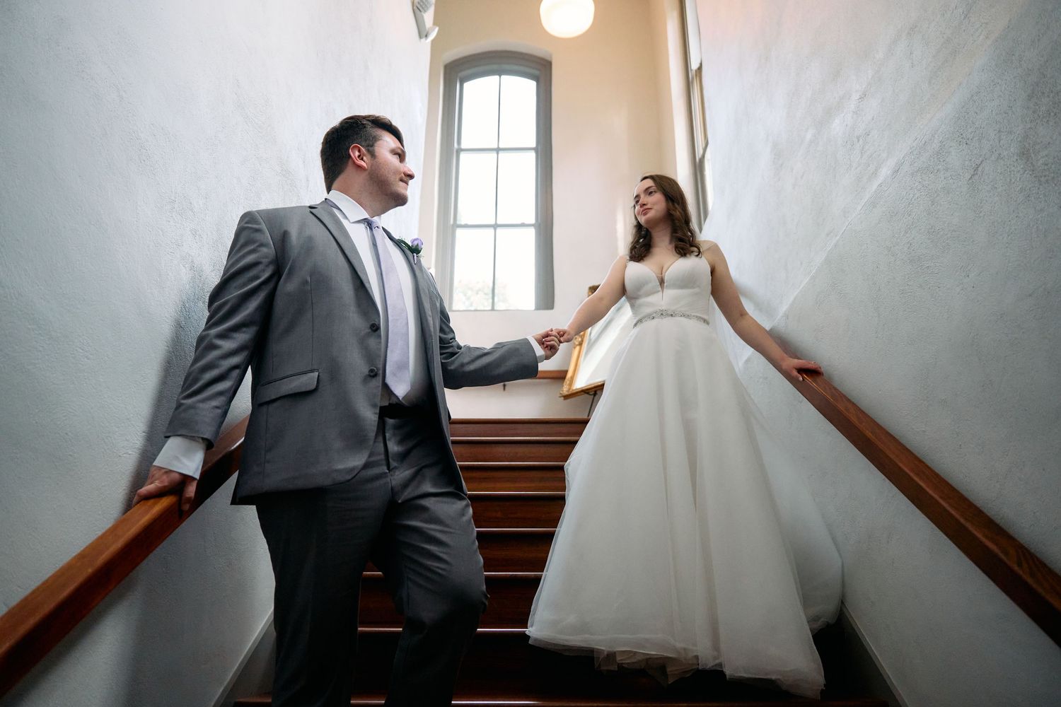 Newlywed couple on a staircase with natural light coming through arched window.
