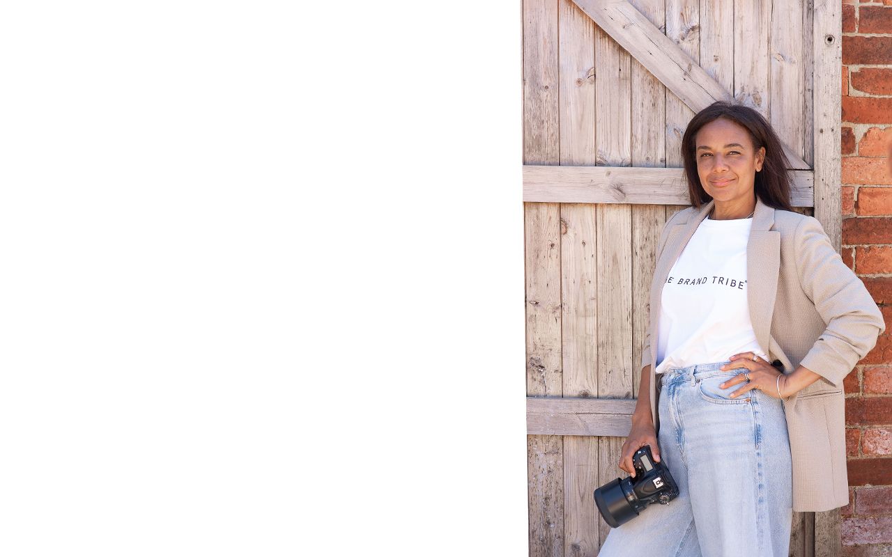 Person wearing a light gray sweatshirt poses casually against a rustic wooden and brick wall background.