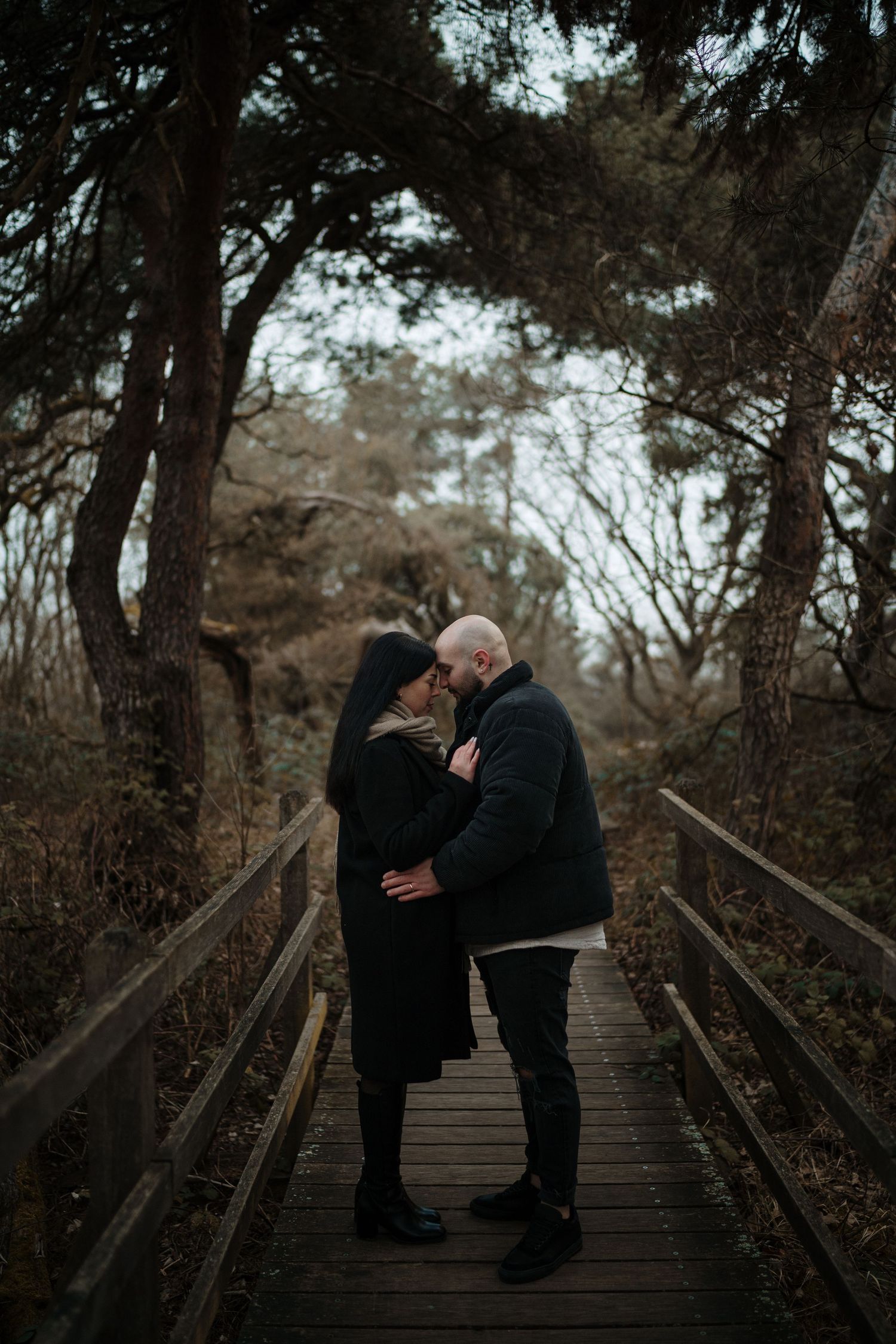 Couple embracing on rustic wooden walkway in forest setting.