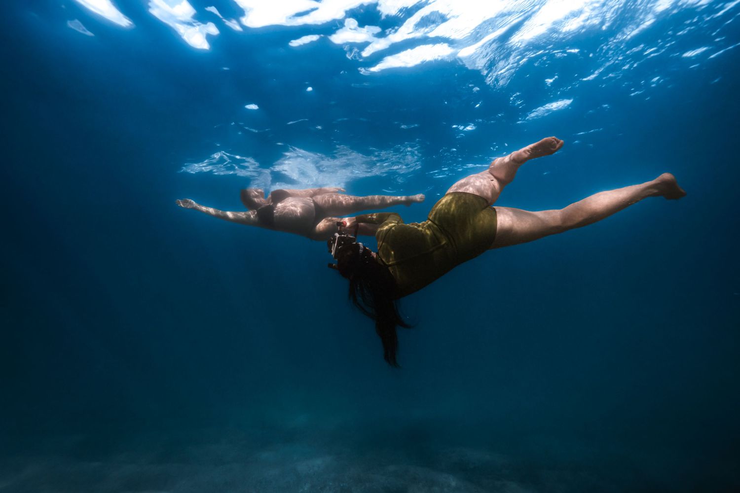 Woman in yellow swimsuit gracefully diving underwater in clear blue ocean.