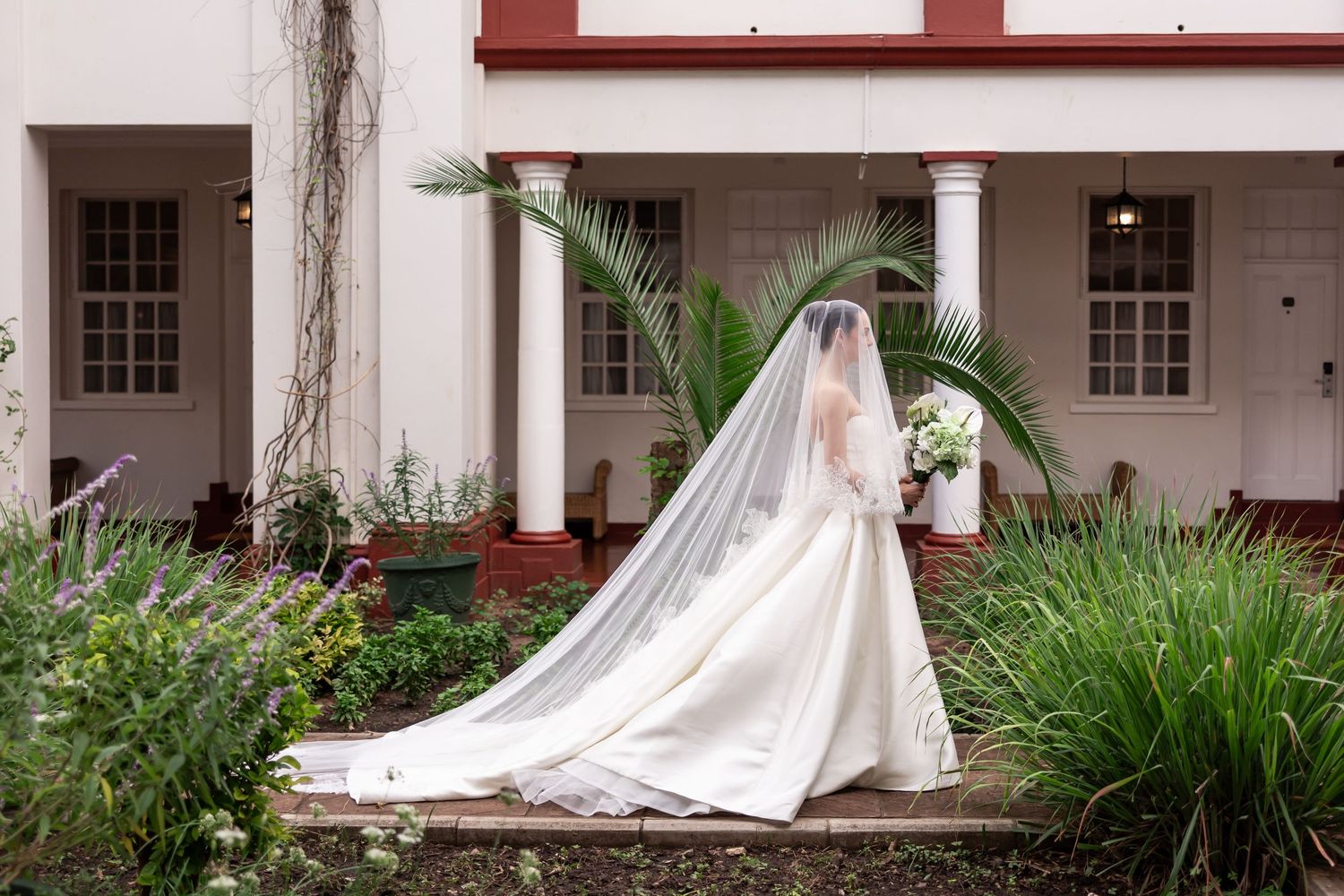 Long white wedding dress train flowing against colonial style architecture. Wedding captured in Victoria Falls - JCclick Wedding photo & Fil