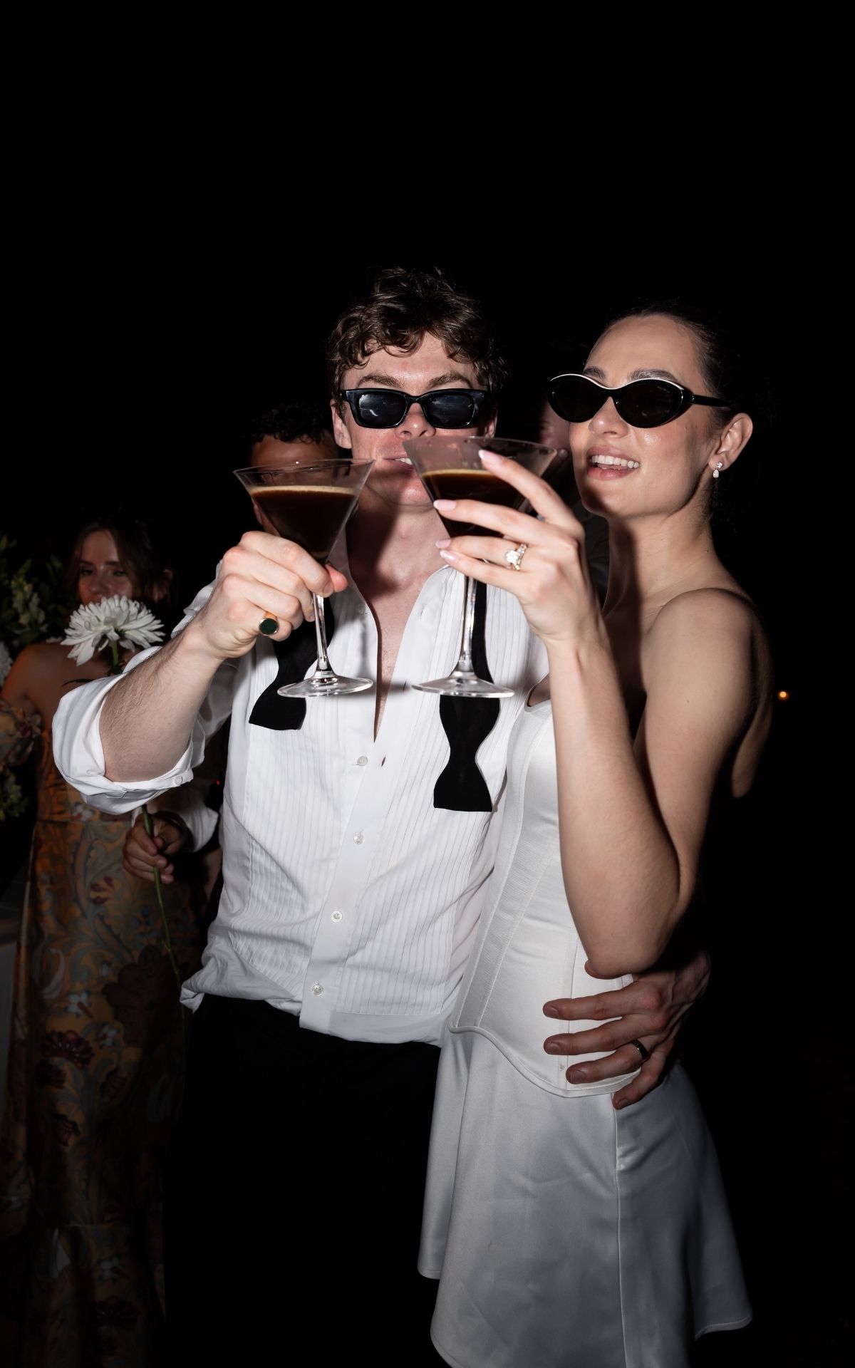 Party guests in formal attire raising glasses for a toast in dark lighting. - JCclick Wedding photo & Film - Best Cape Town Photographer.
