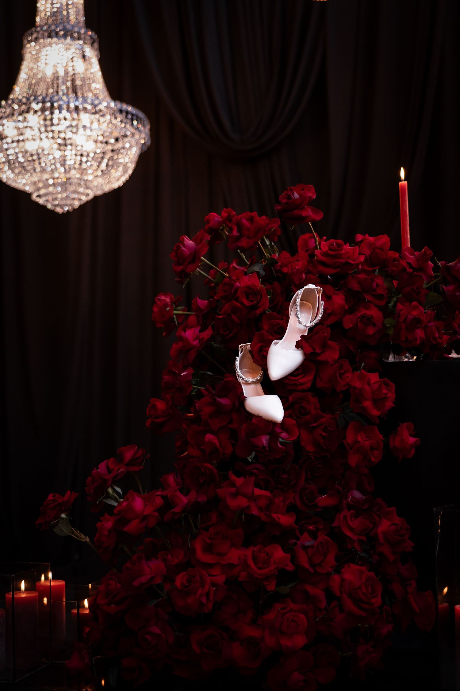 White bridal shoes displayed on red roses under crystal chandelier - JCclick Wedding photo & Film - Best Cape Town Photographer.