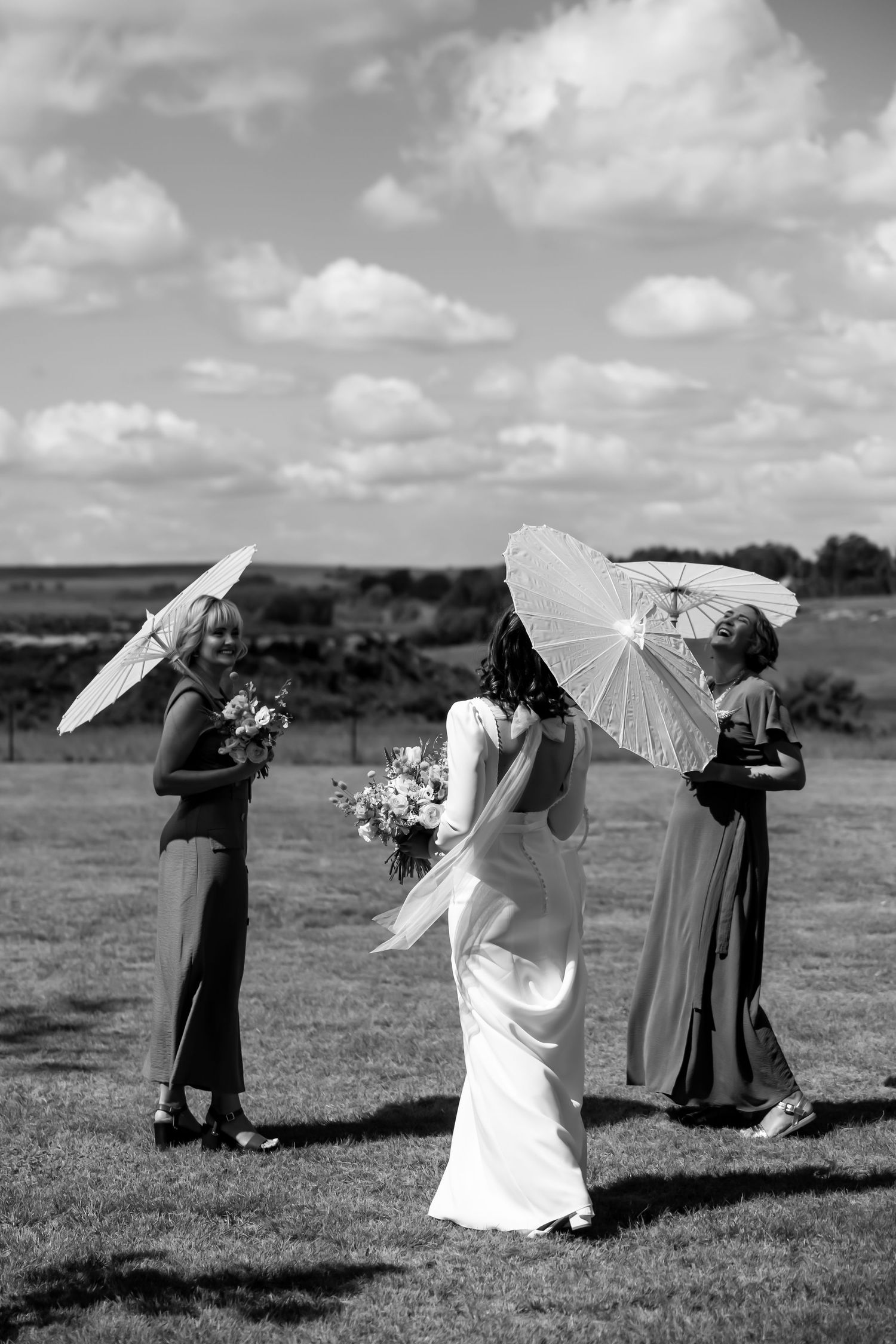 Black and white photo of wedding party with parasols in an open field.  JCclick Wedding photo & Film - Best Cape Town Photographer.