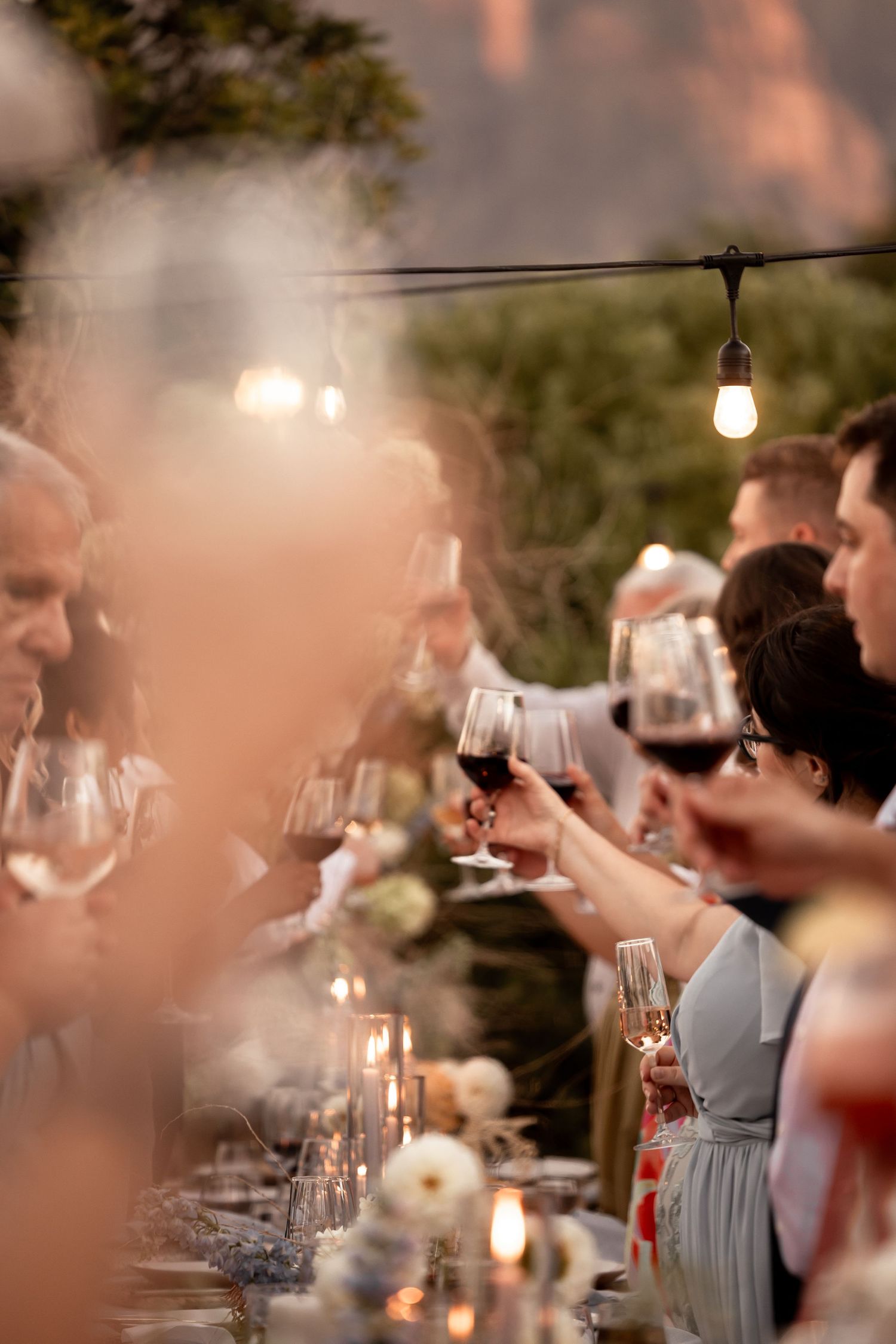 Wedding guests toasting with wine glasses at outdoor reception under string lights. - JCclick Wedding photo & Film - Best Cape Town Photogra