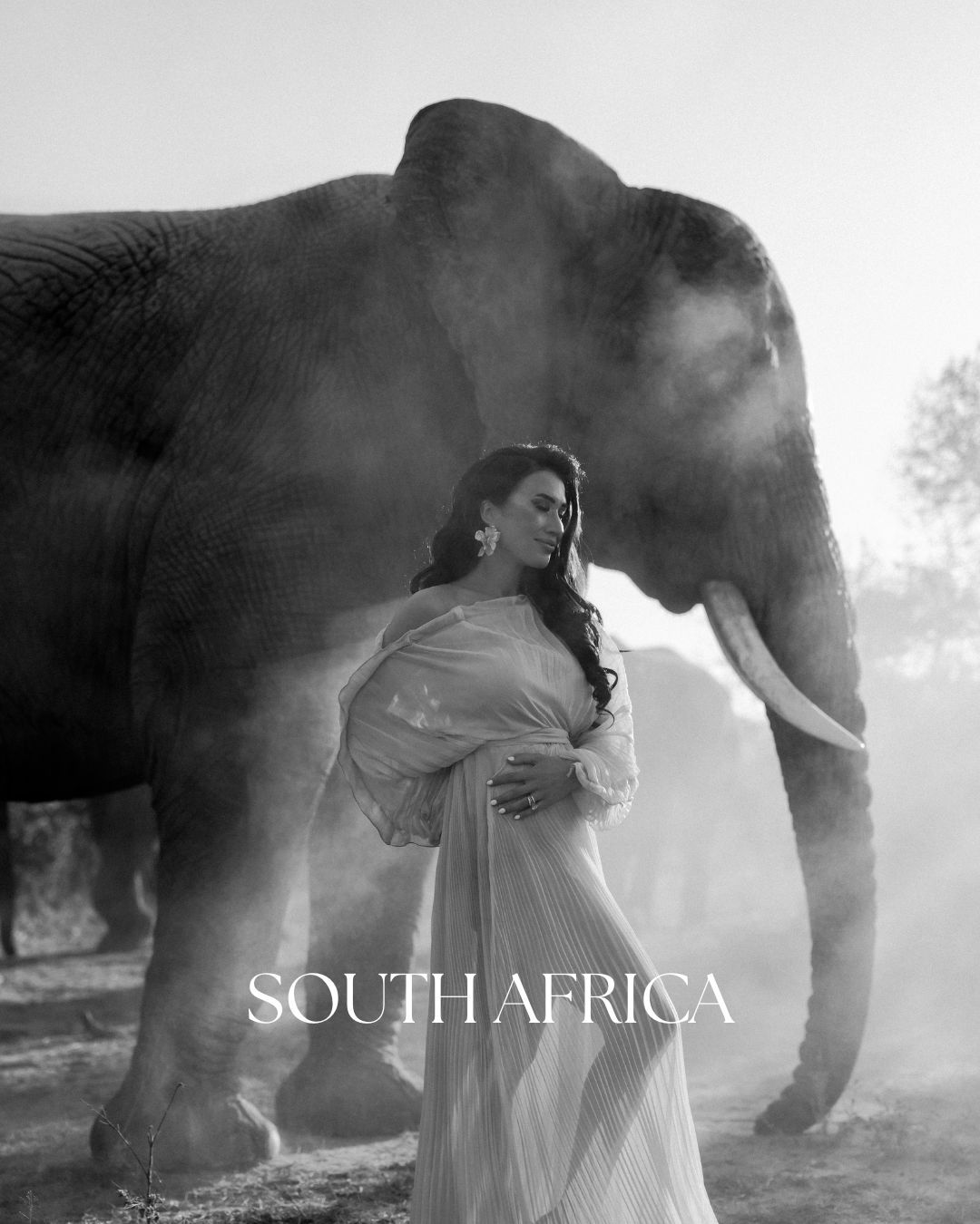 Artistic black and white photo of a woman in flowing dress posing with an elephant in South Africa. - JCclick Wedding photo & Film - Best Ca