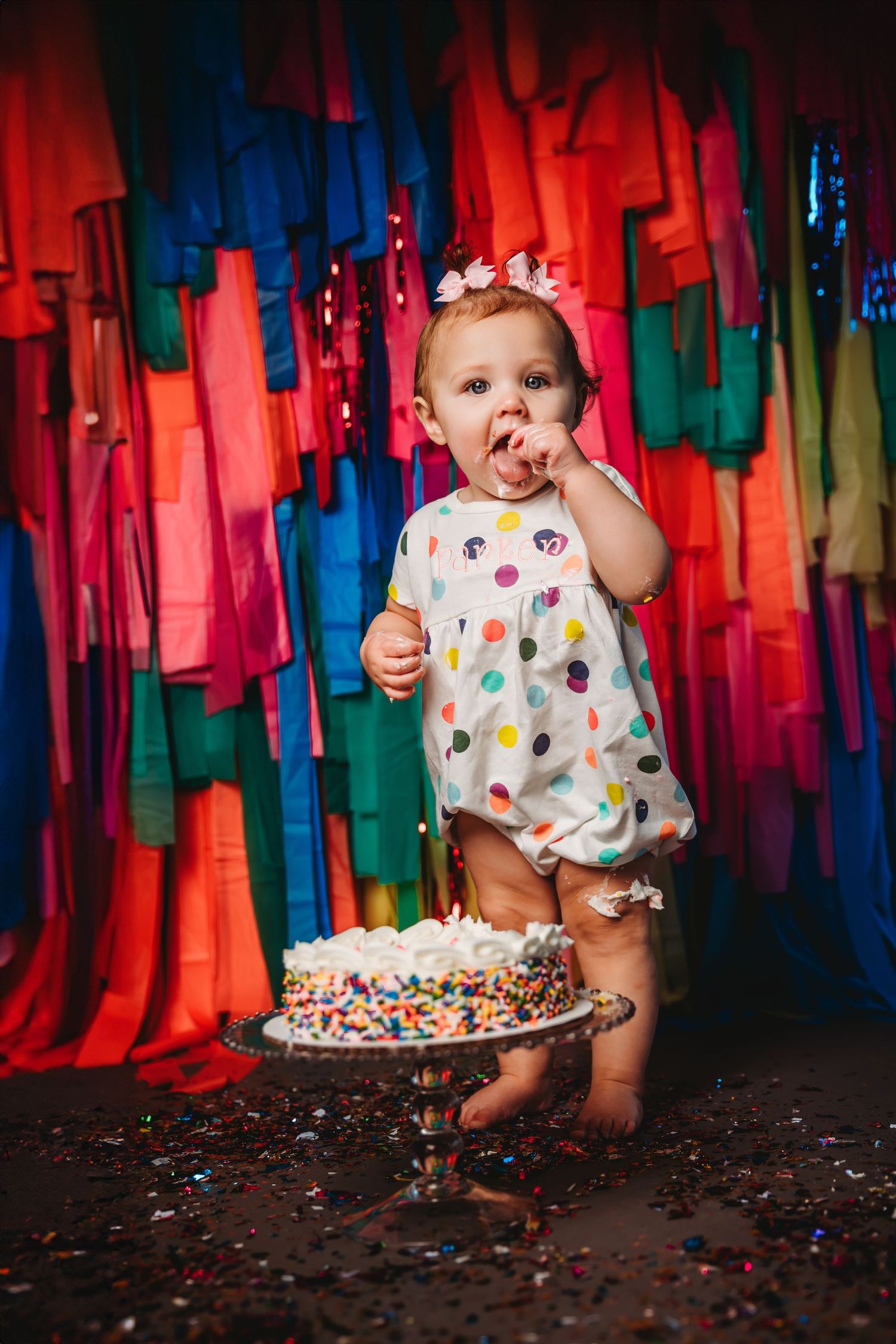 Colorful cake smash photo session with streamers and sprinkles for celebrating milestone.