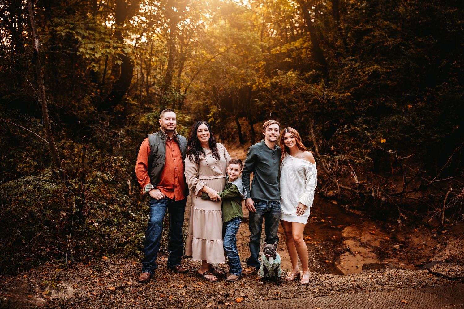 Family of five posing outdoors in a sunlit forest setting during a professional fall photo session.