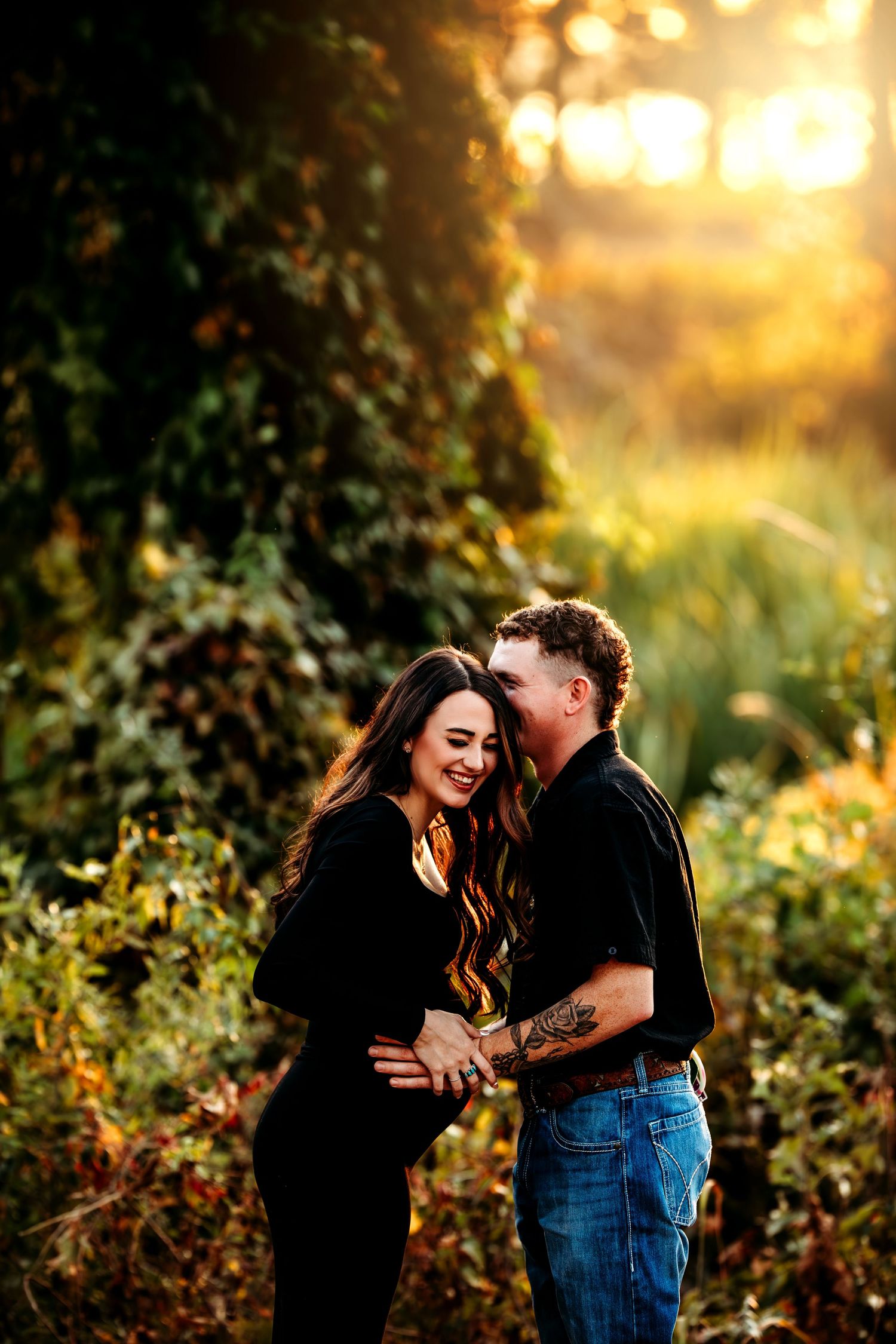 A couple shares intimate moments at sunset in a garden setting with golden bokeh lighting and greenery.